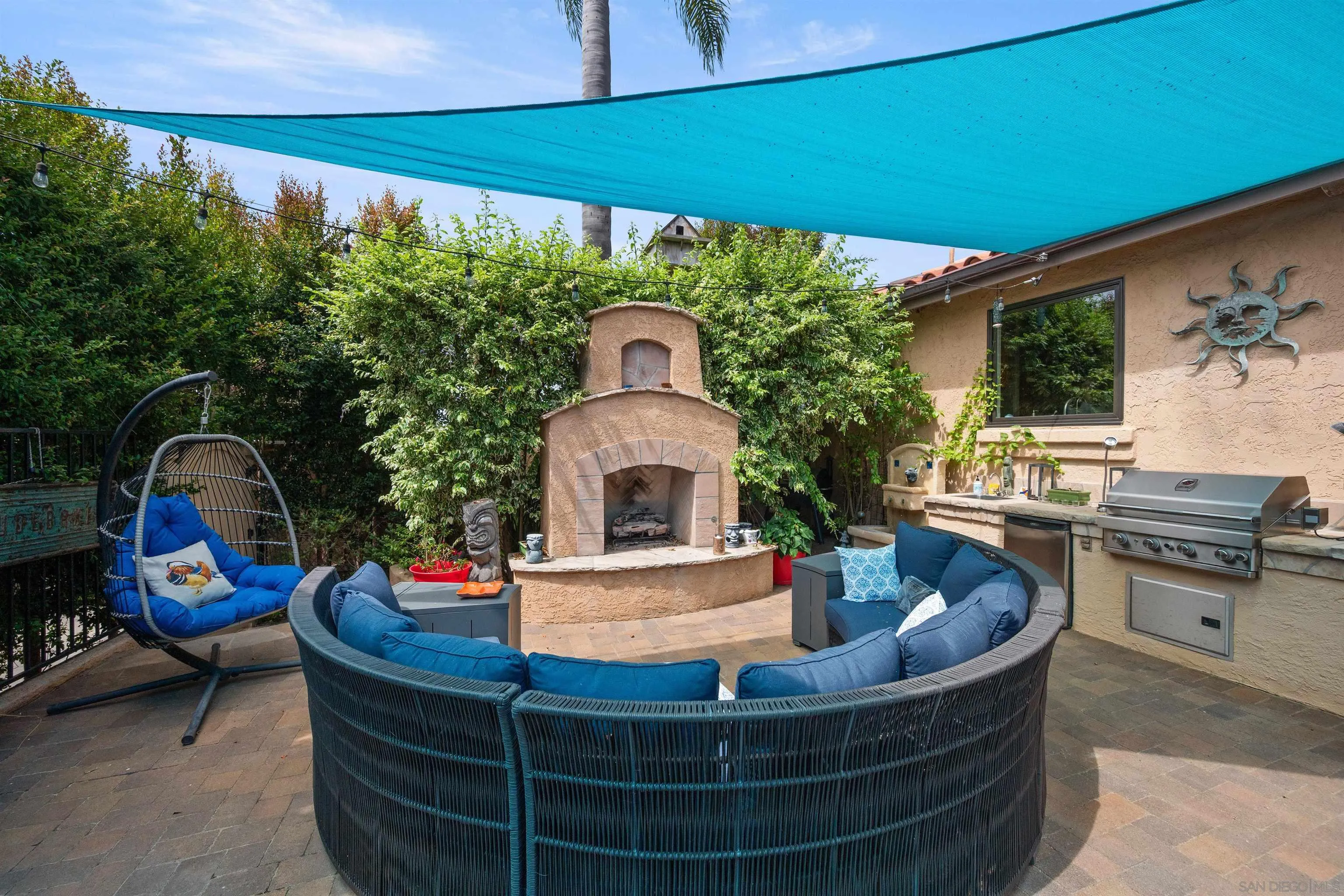 Outdoor patio with a turquoise shade sail, cushioned seating, stucco fireplace, and built-in grill.
