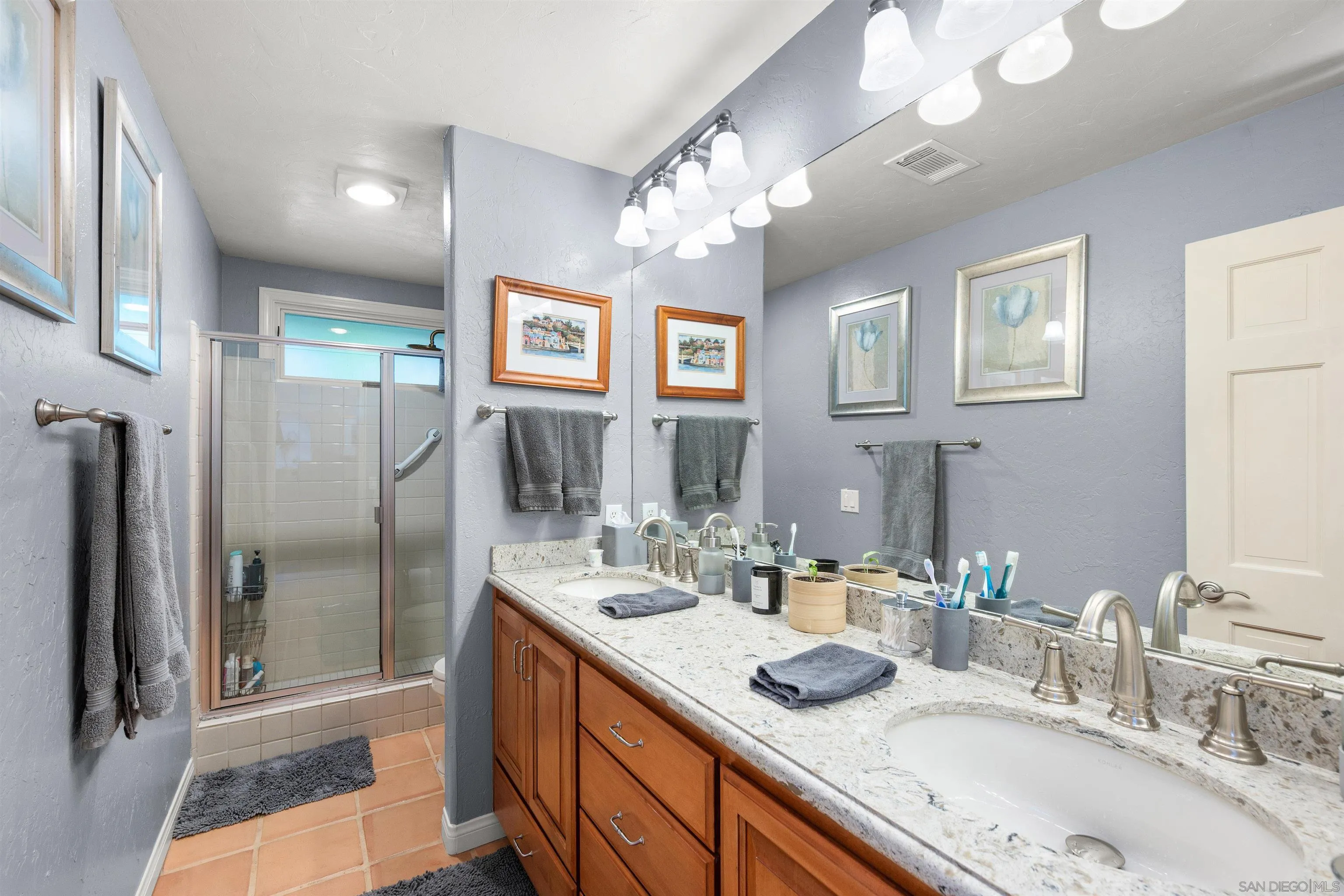 Bathroom with double vanity and granite counter beside a glass-enclosed tiled shower.