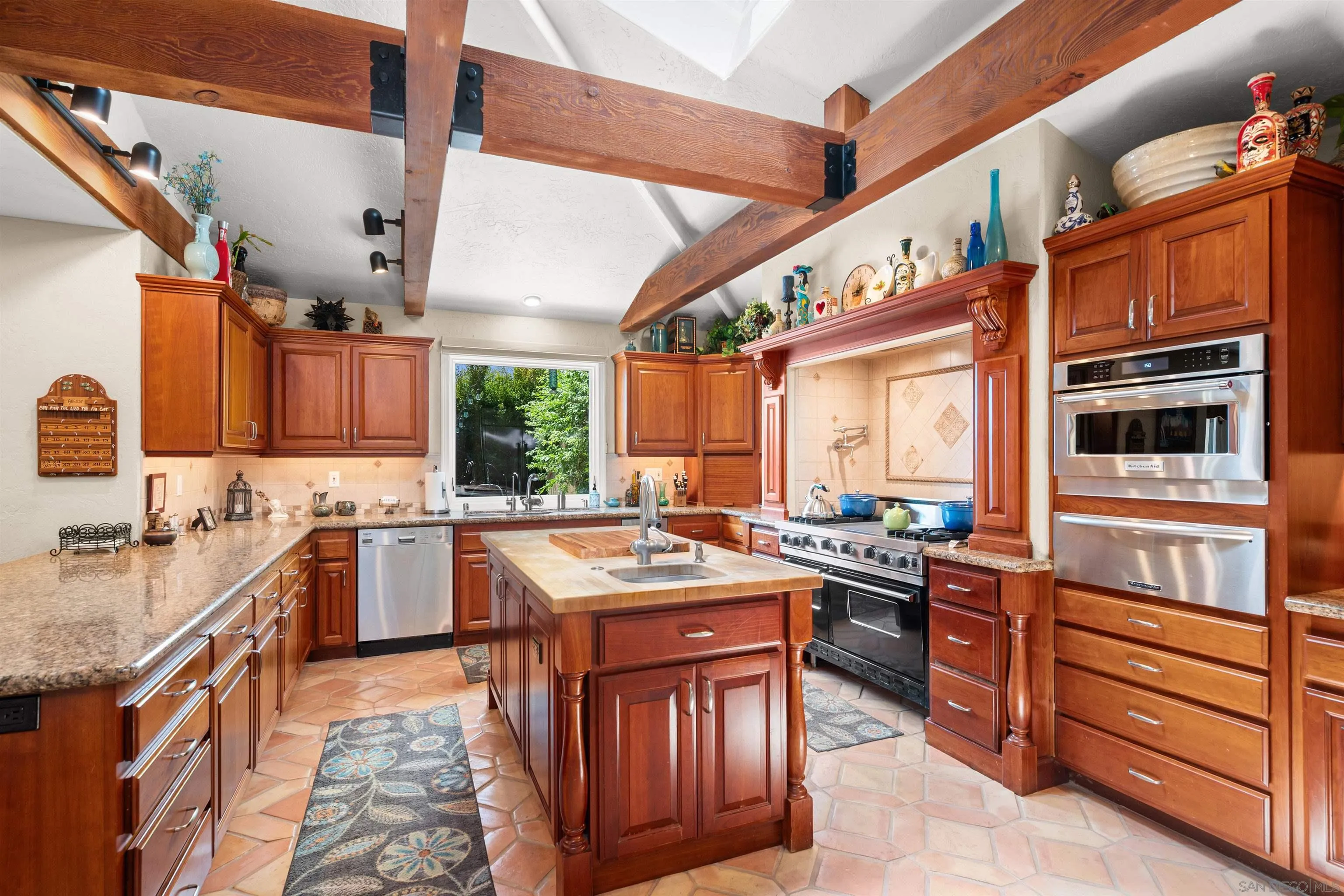 Kitchen with a wood island, extensive cabinetry, stainless steel appliances, and exposed ceiling beams.