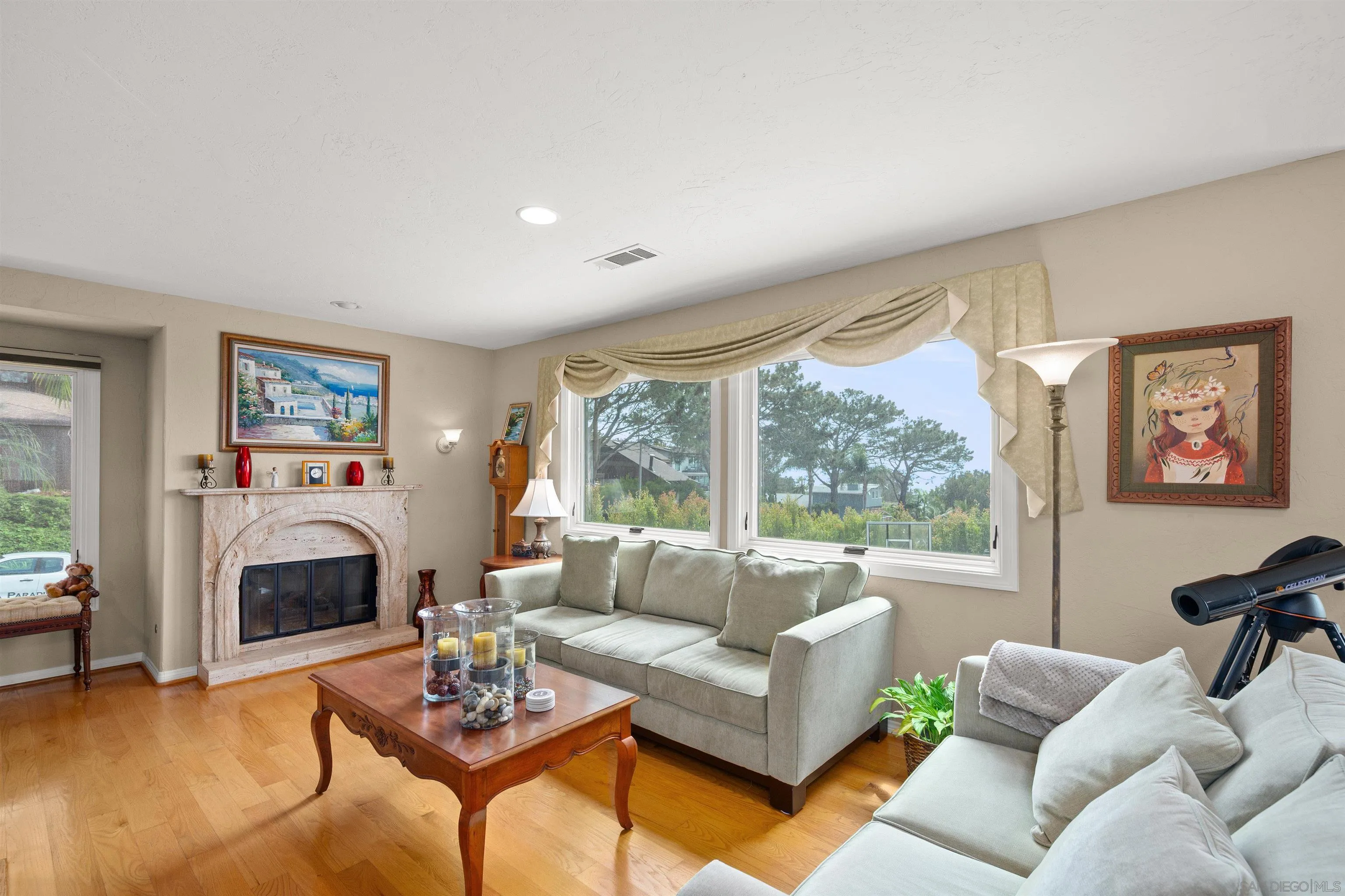 Living room with a stone fireplace, large curtained window, hardwood floors, and light sofas.