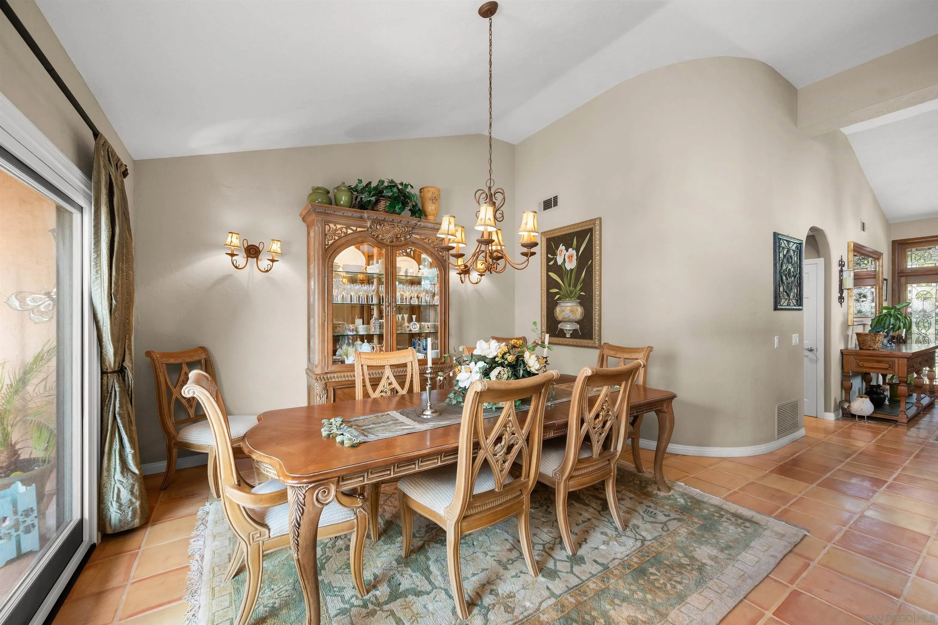 Dining room with ornate wooden furniture, a glass-front china cabinet, and terracotta tile flooring.
