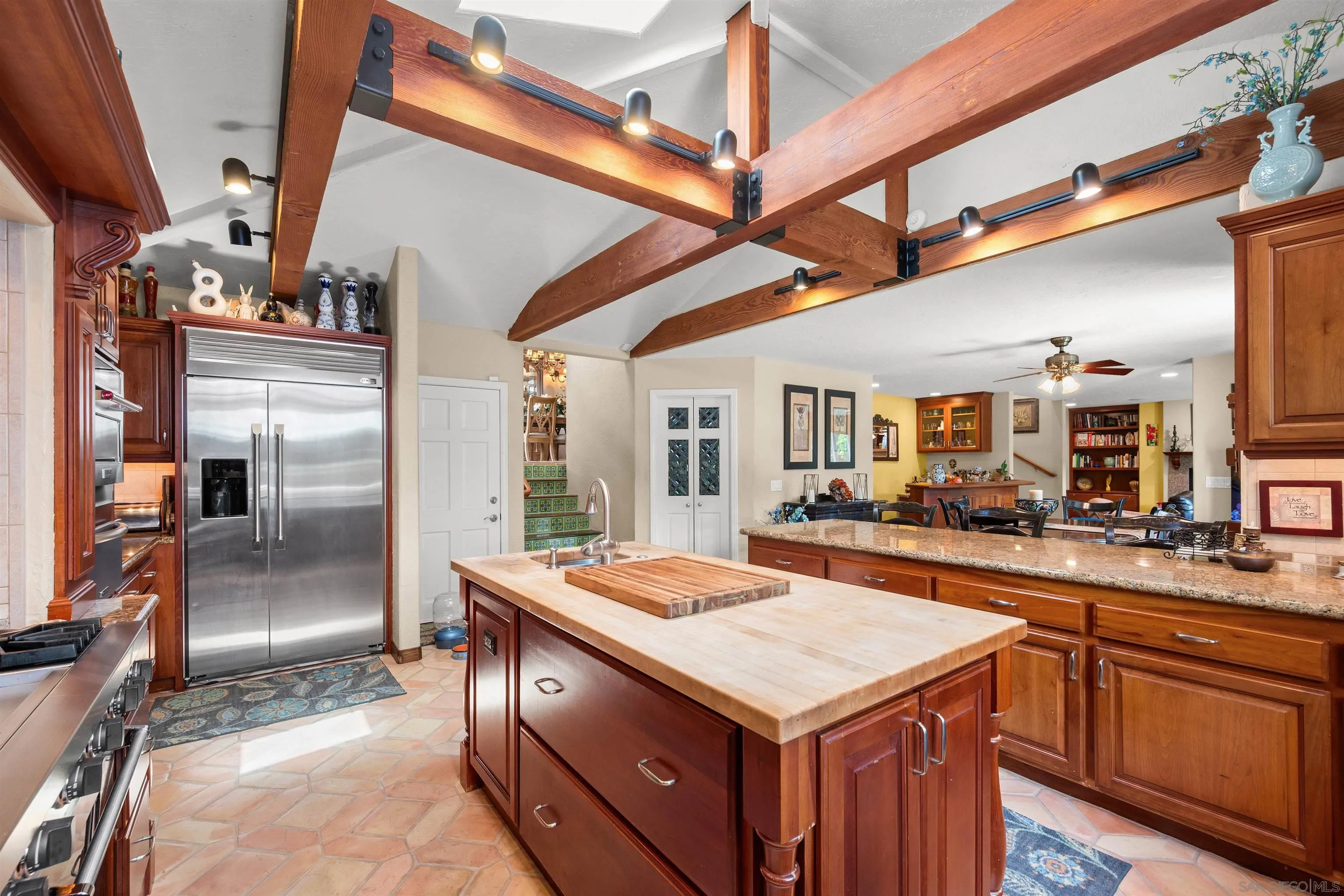 Kitchen with a butcher-block island, cherry cabinetry, stainless appliances, and exposed timber ceiling beams.