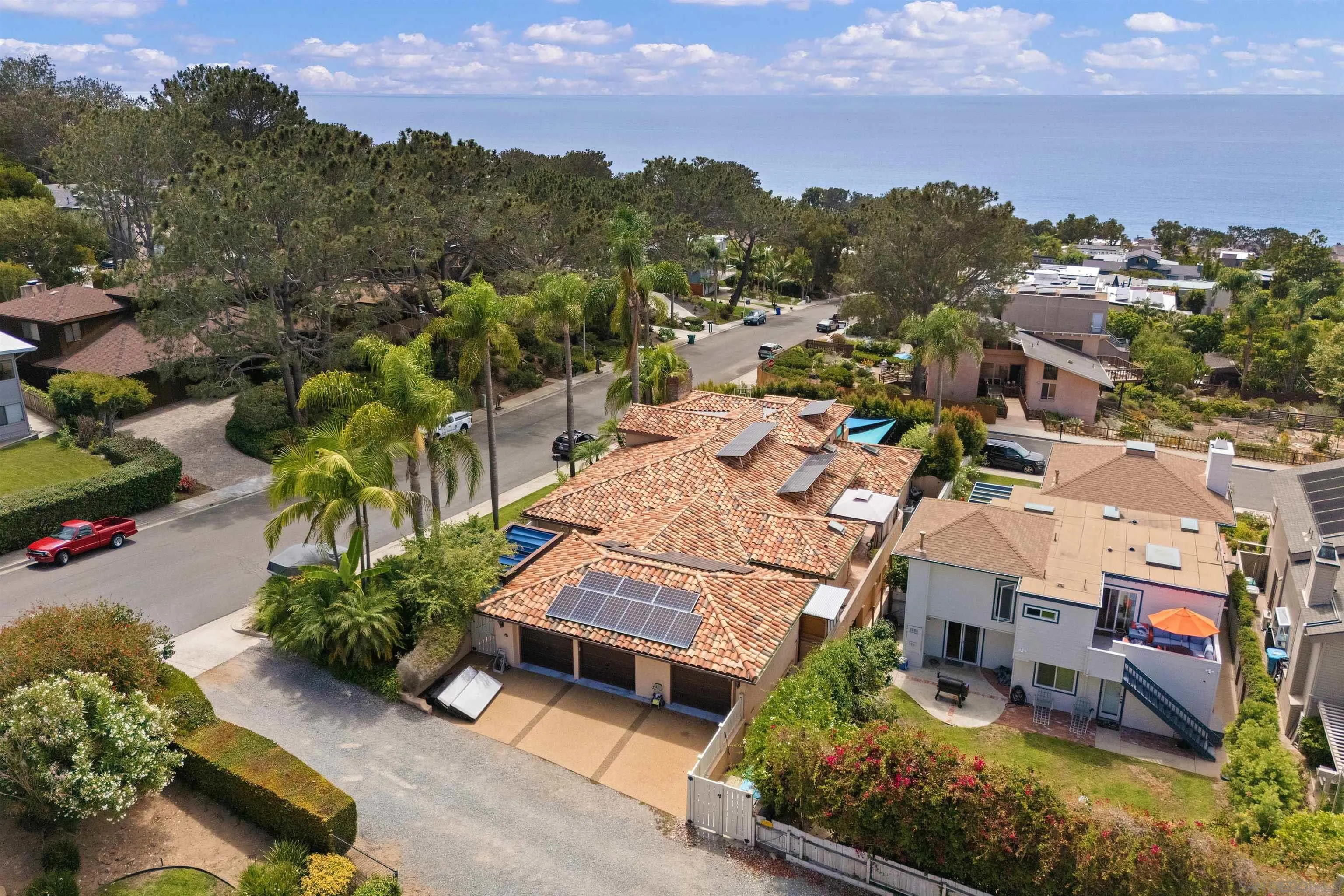 Aerial view of a solar-paneled terracotta-roof home, with the Pacific Ocean beyond the neighborhood.