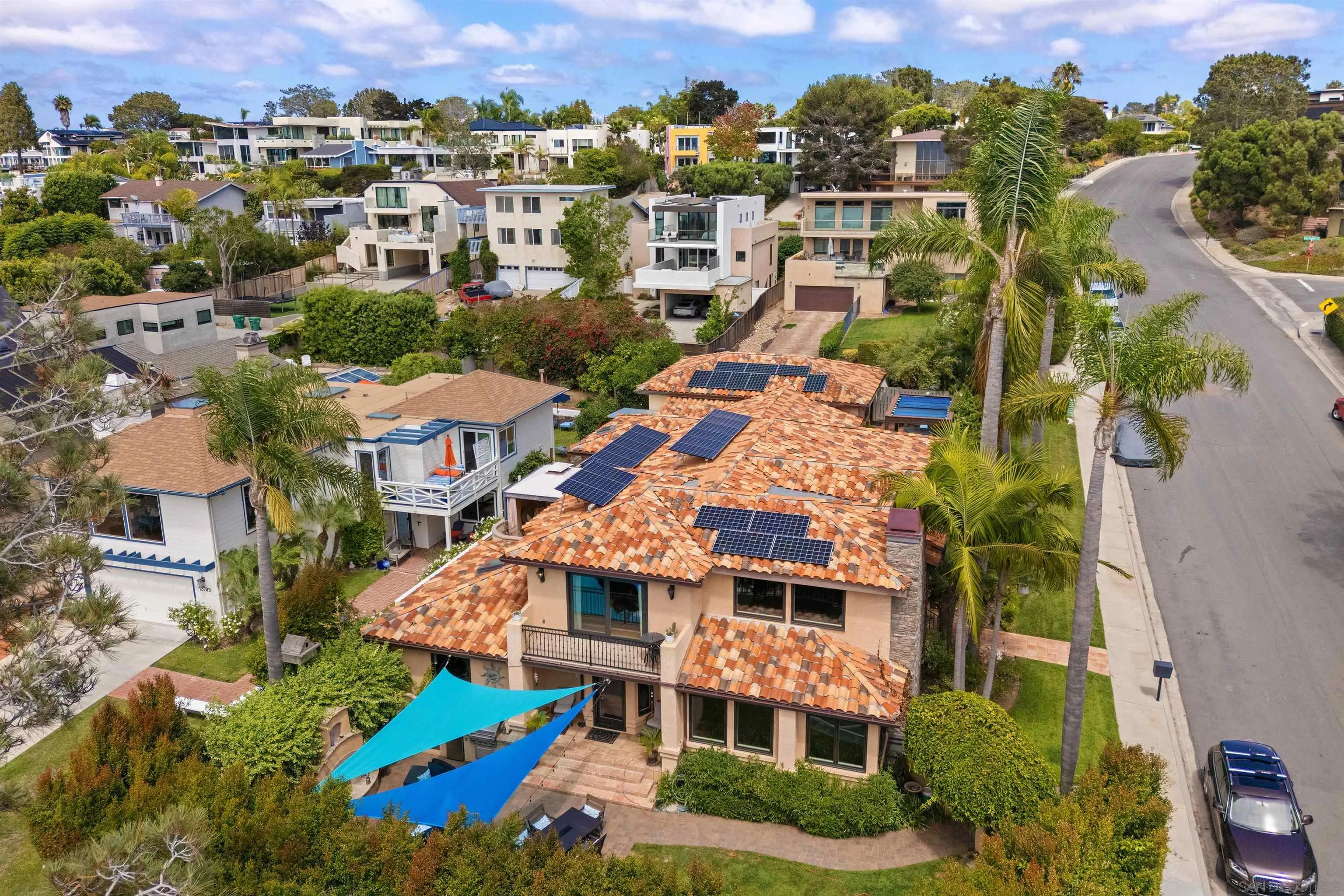 Aerial view of a Del Mar home with solar panels, terracotta roof tiles, and blue backyard shade sails.