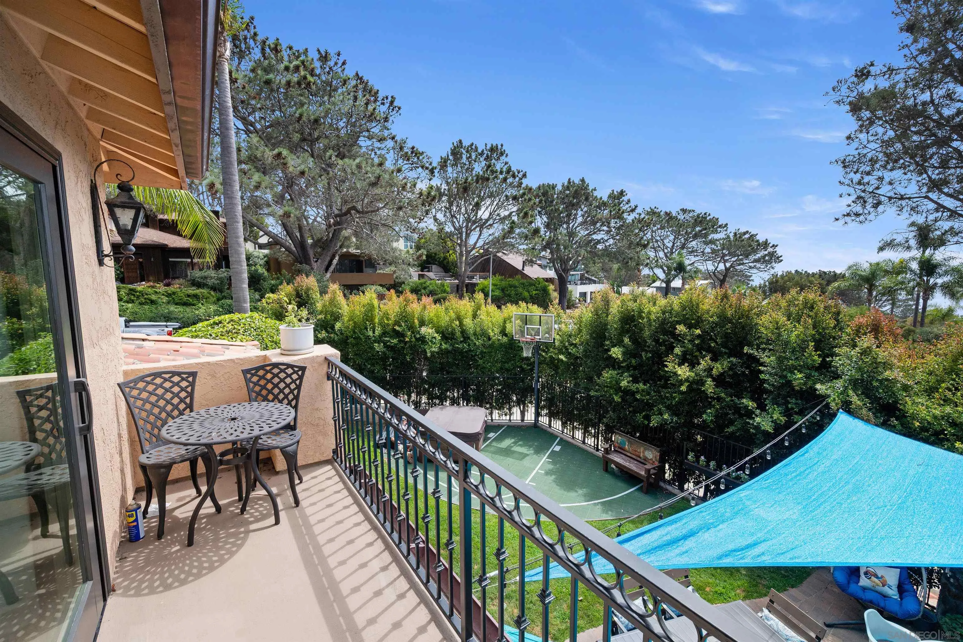 Furnished balcony overlooking a backyard basketball court and blue shade sail