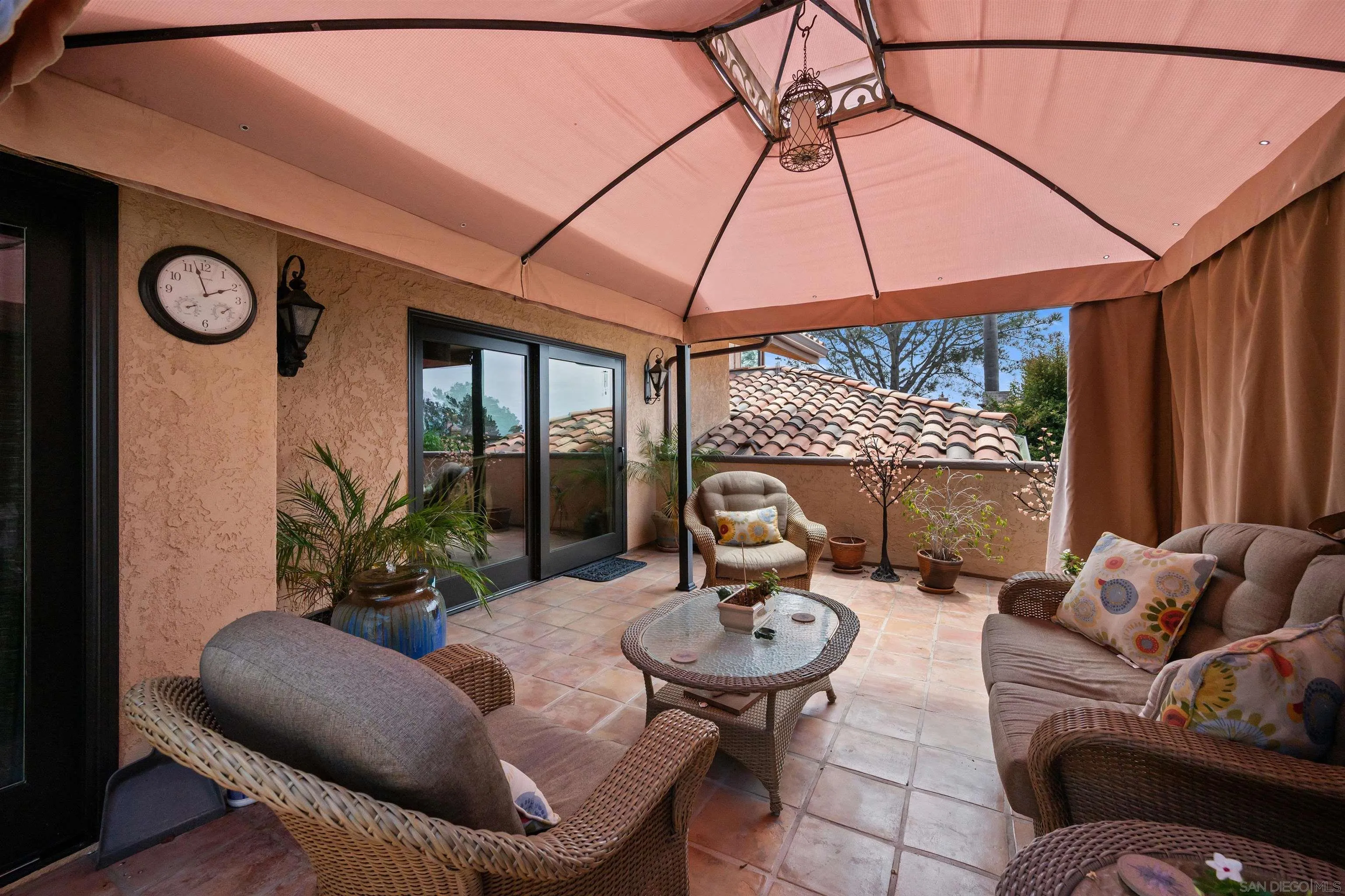 Covered patio with wicker seating, terracotta tile, potted plants, and a large shade canopy.