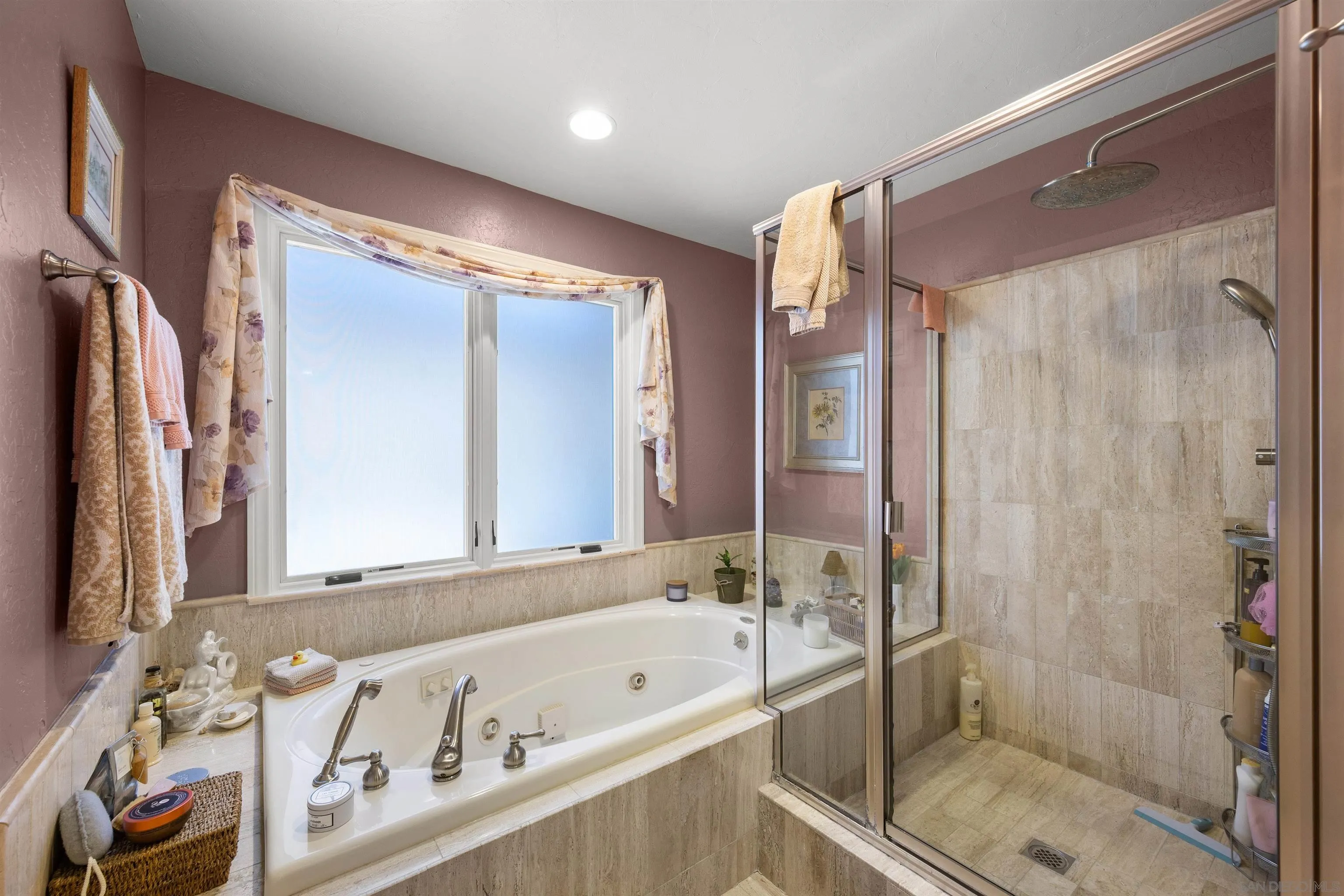 Bathroom with a jetted soaking tub beneath a wide window and a glass-enclosed tiled shower.