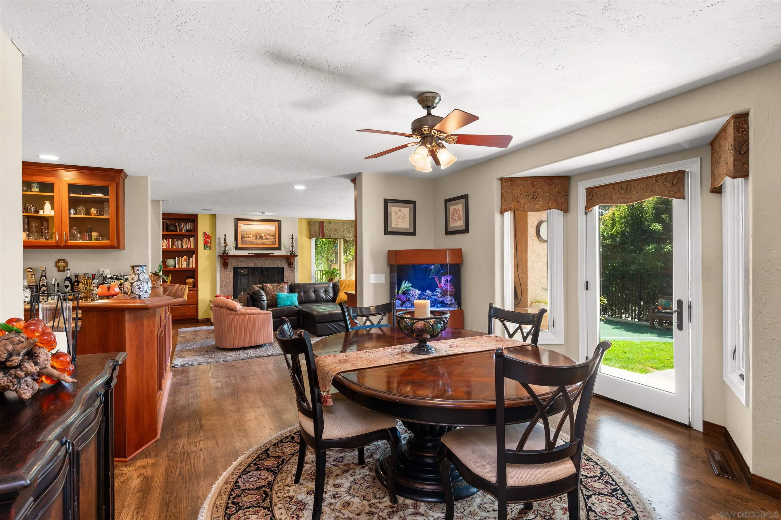 Dining area with a round wooden table, opening into a furnished living room with a fireplace and aquarium.
