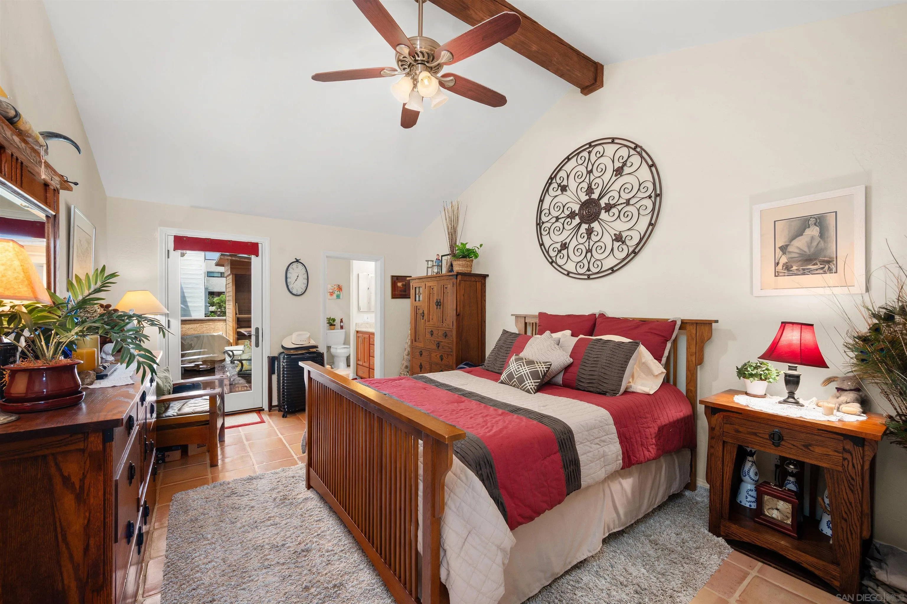 Furnished bedroom with a red-and-gray bed, vaulted ceiling, ceiling fan, and glass door to the outdoors.