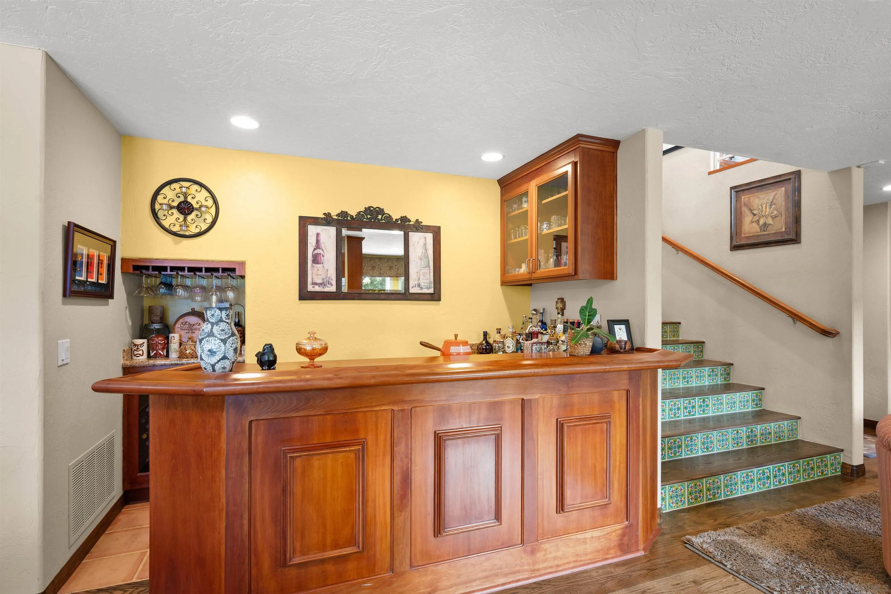 Wooden home bar beside a staircase with colorful patterned tile risers.