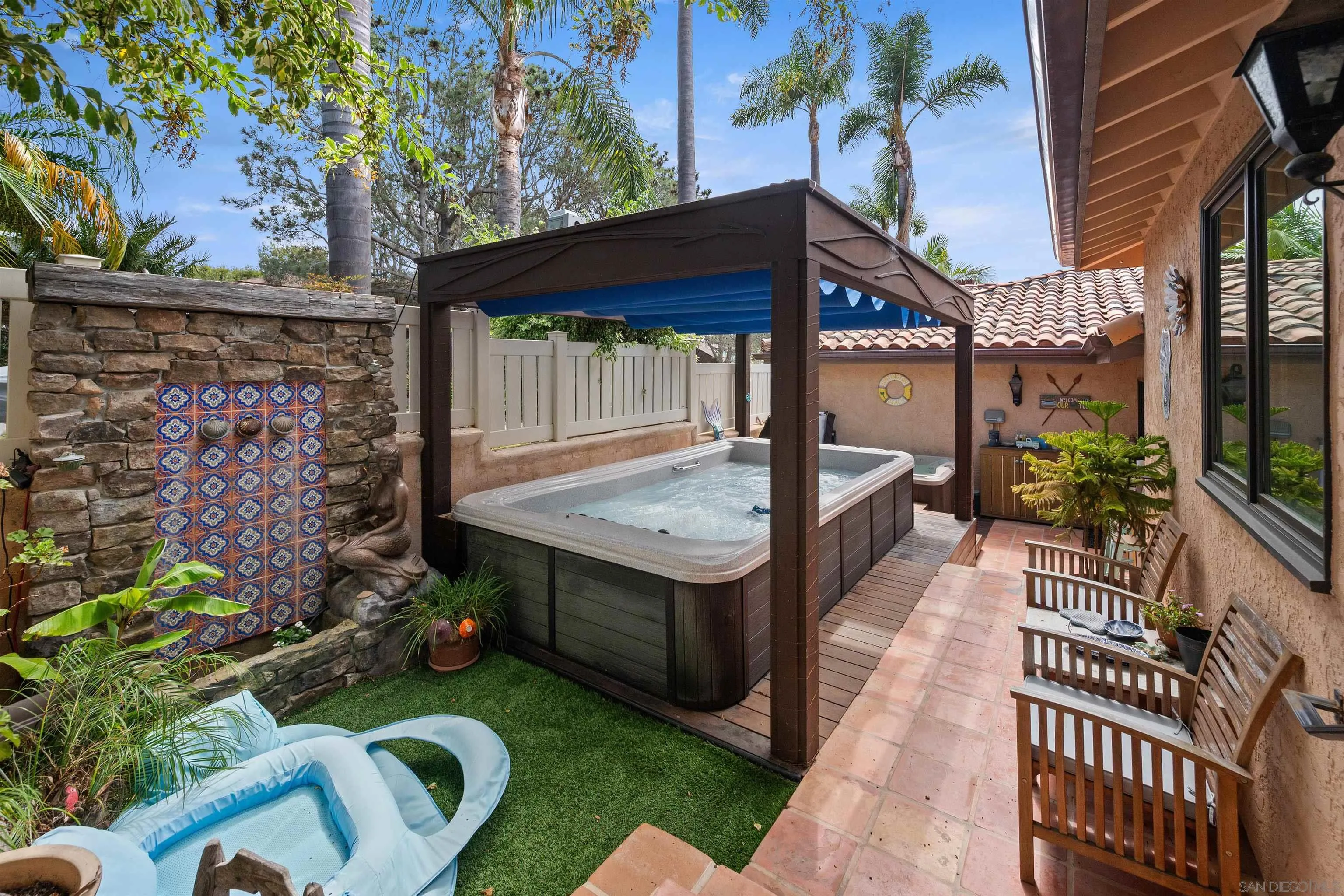 Outdoor patio with a hot tub under a pergola, colorful tiled water feature, and wooden benches.