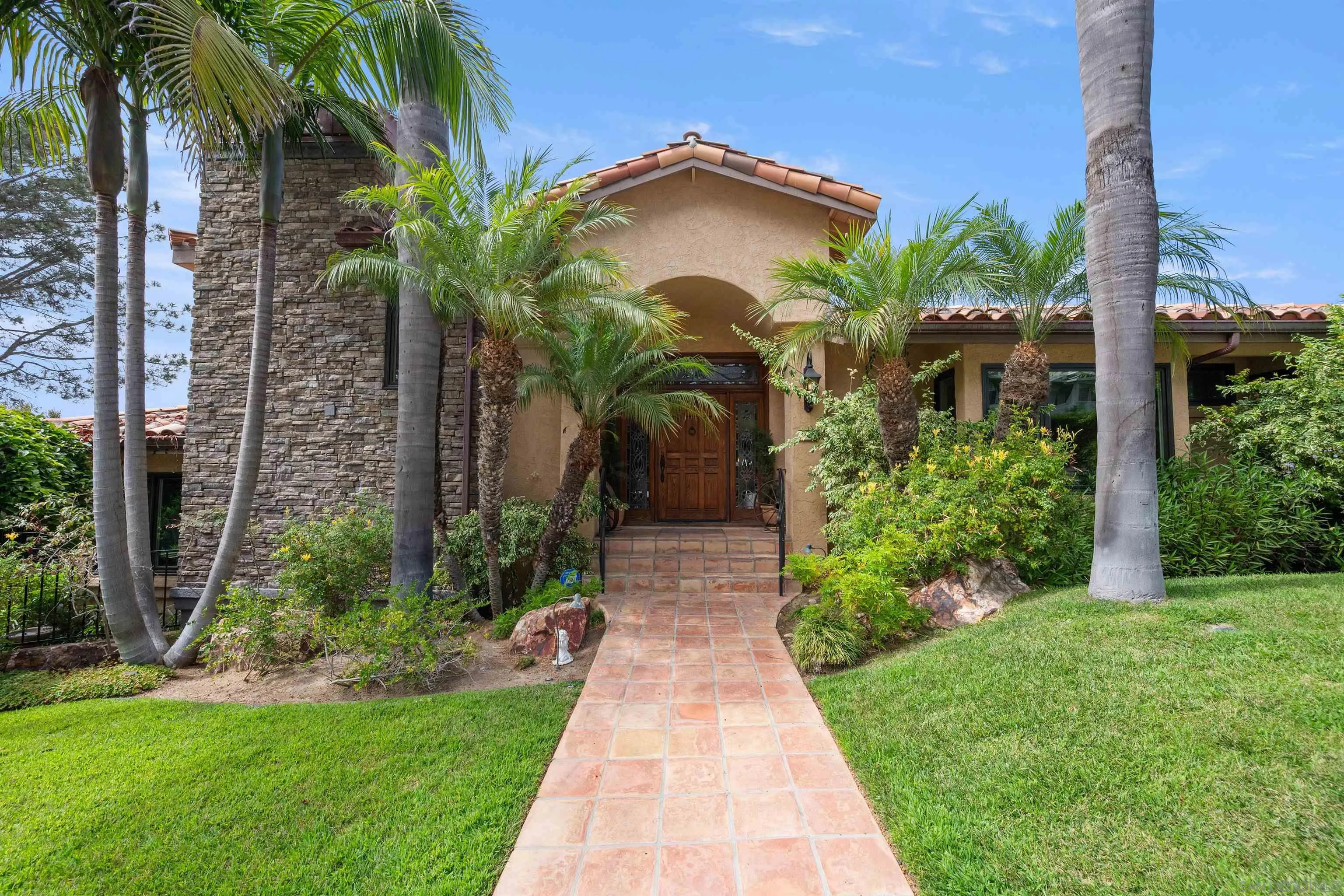 House entrance with stone tower, tiled walkway, and palm trees.