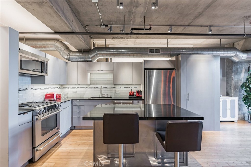 Industrial-style kitchen with stainless-steel appliances, dark island, and exposed concrete ceiling.