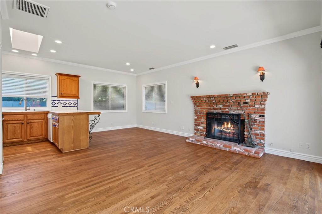 Unfurnished living area with hardwood floors, a brick fireplace, and a small wood-cabinet kitchenette.