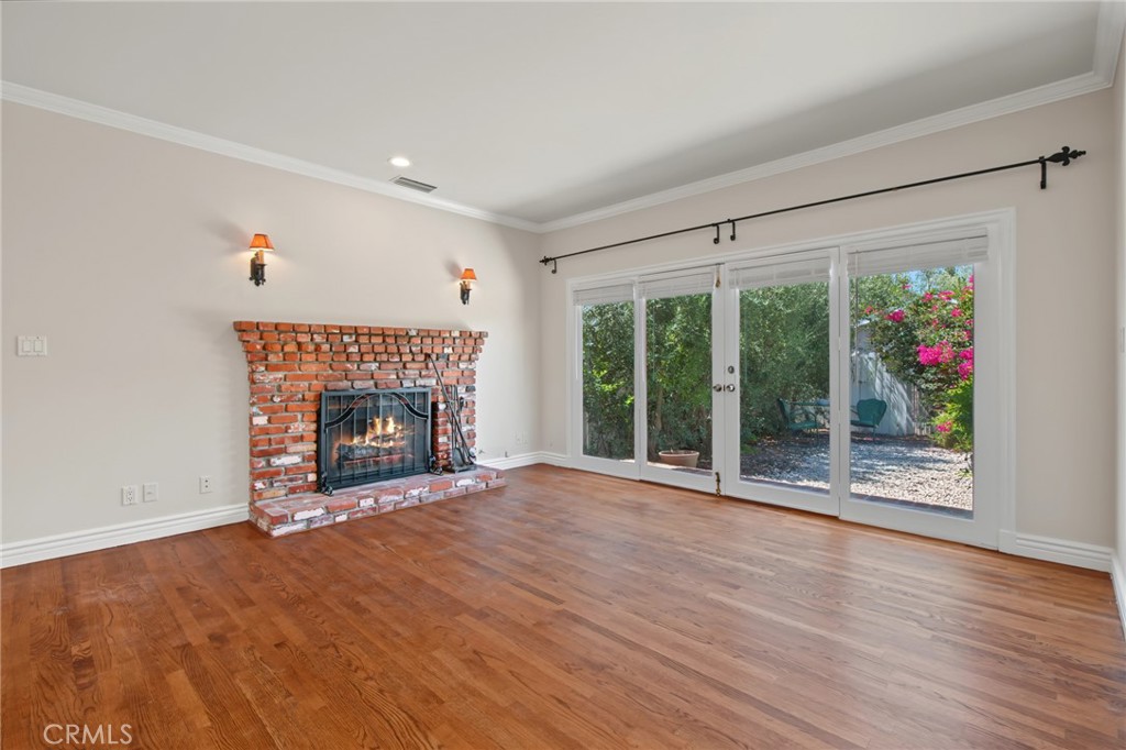 Empty living room with a brick fireplace, hardwood floors, and sliding glass doors to a garden.