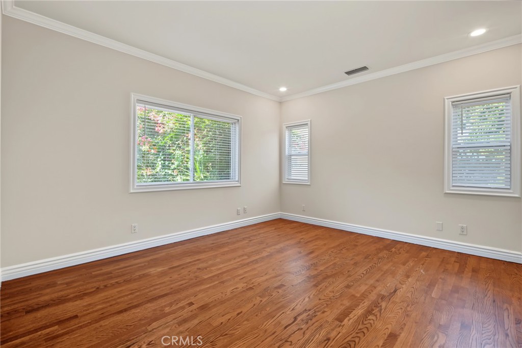 Empty room with hardwood floors, crown molding, and three windows with blinds.