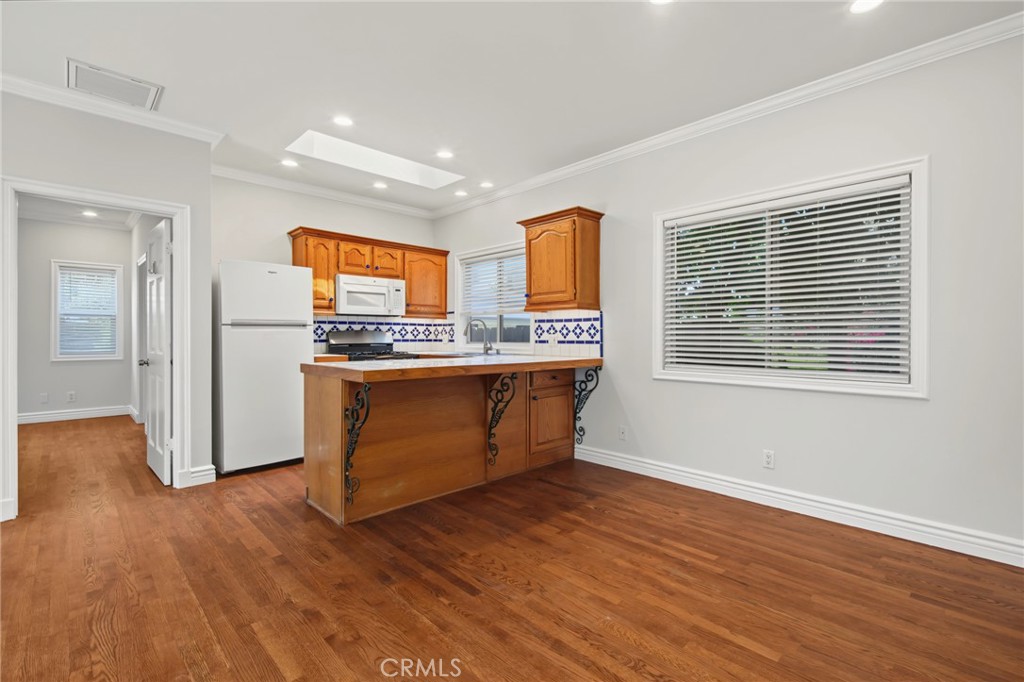 Kitchen with warm wood cabinetry, white appliances, tiled backsplash, and hardwood floors.