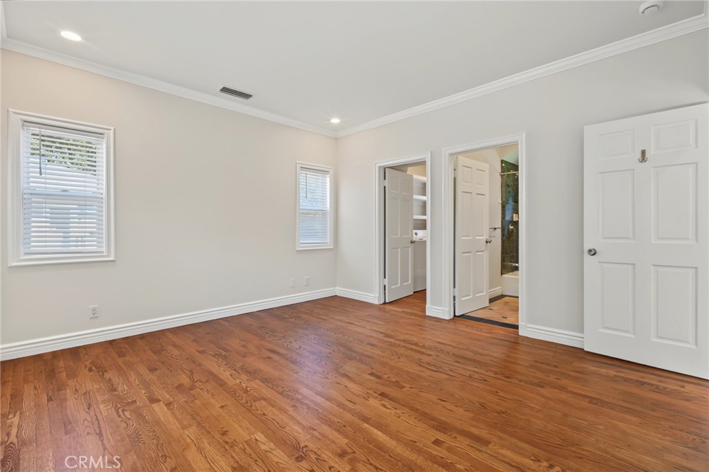 Empty bedroom with hardwood floors, crown molding, and two windows.