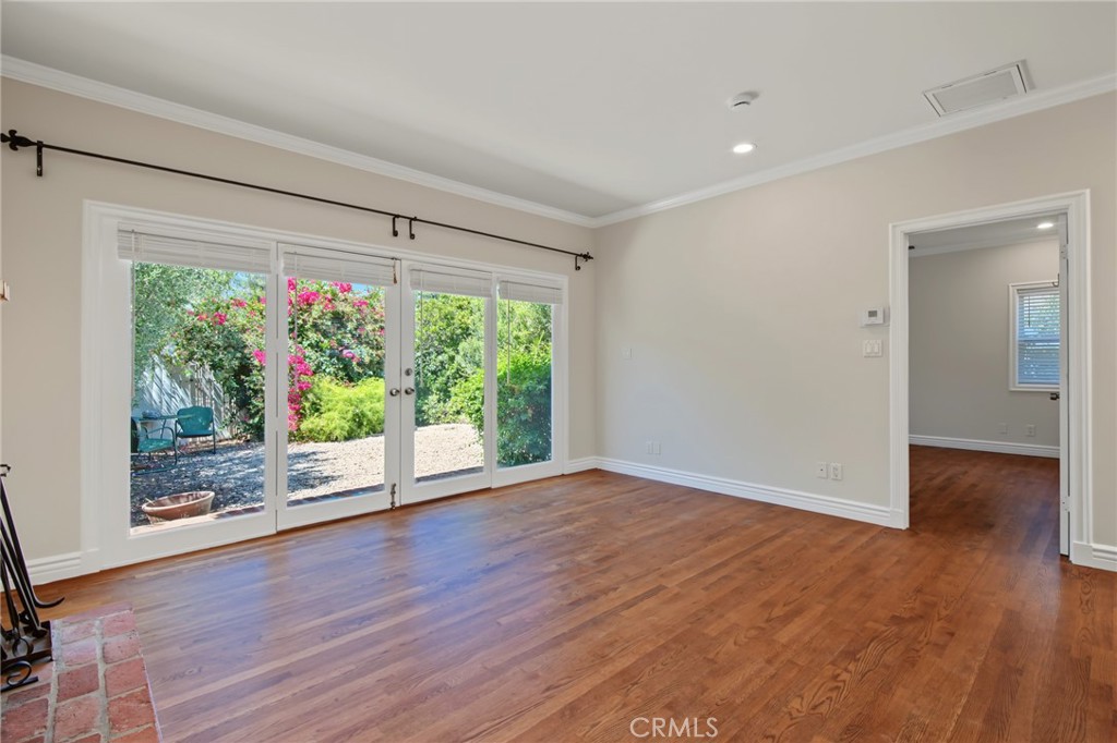 Empty living room with hardwood floors, glass garden doors, and a brick fireplace edge.