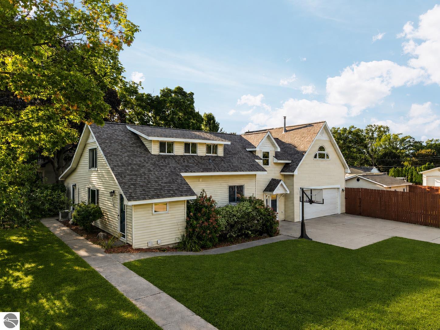 Cream-colored gabled house with a garage, broad lawn, mature trees, and a basketball hoop.
