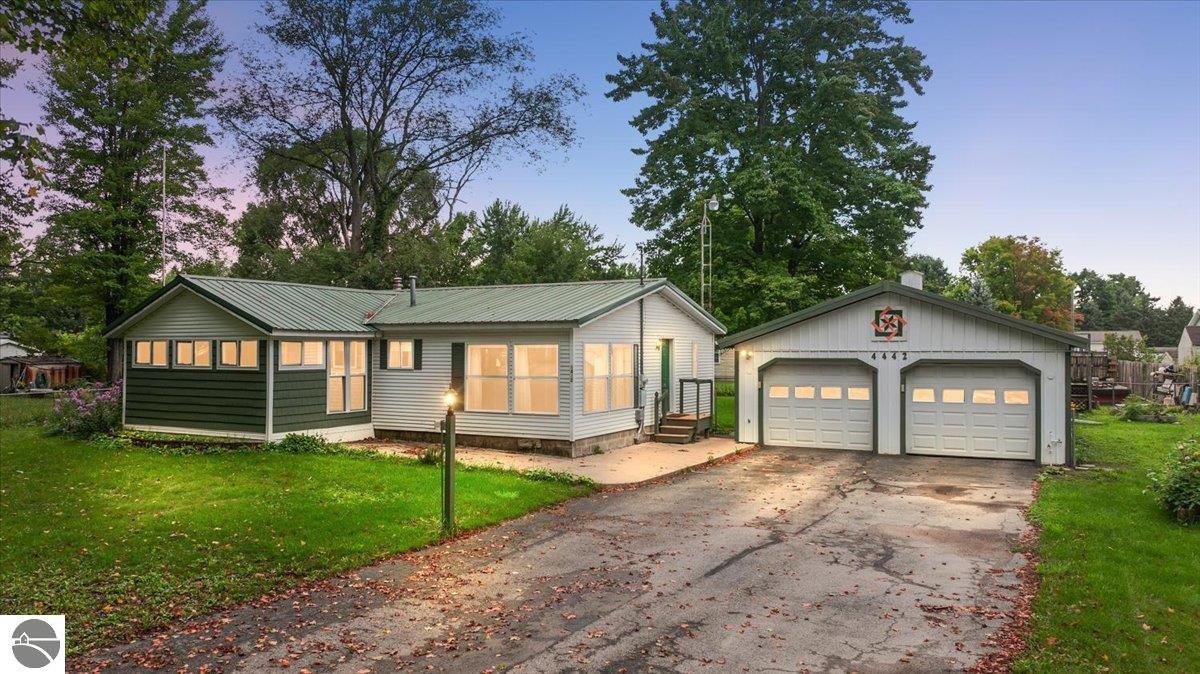 Single-story home with a green metal roof and detached two-car garage, viewed from the driveway at dusk.