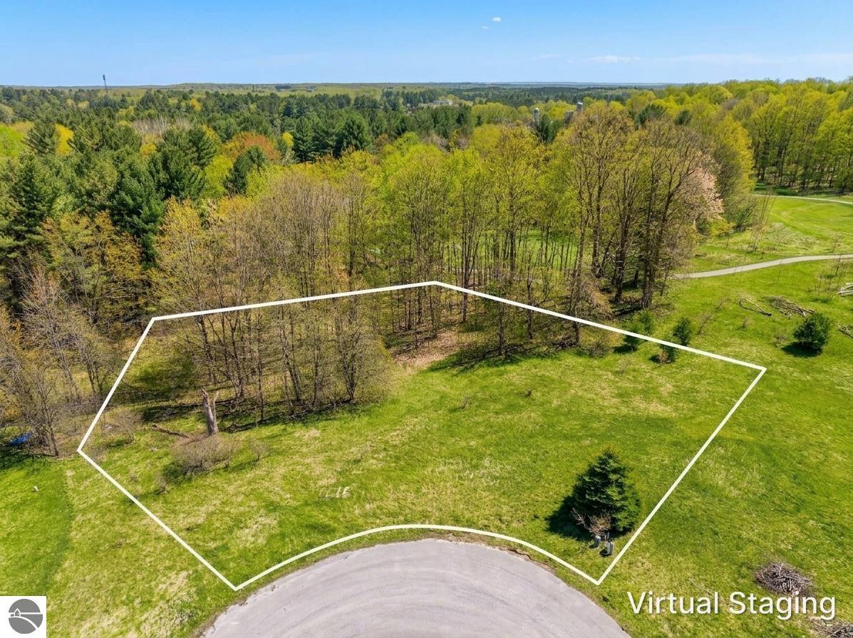 Aerial view of a grassy parcel outlined in white beside woods and a curved road.