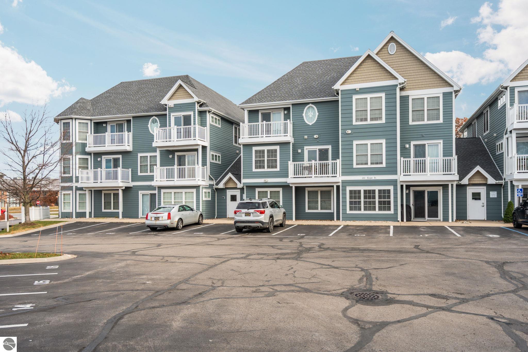 Blue-gray multi-story residential building with white balconies and a paved parking lot.