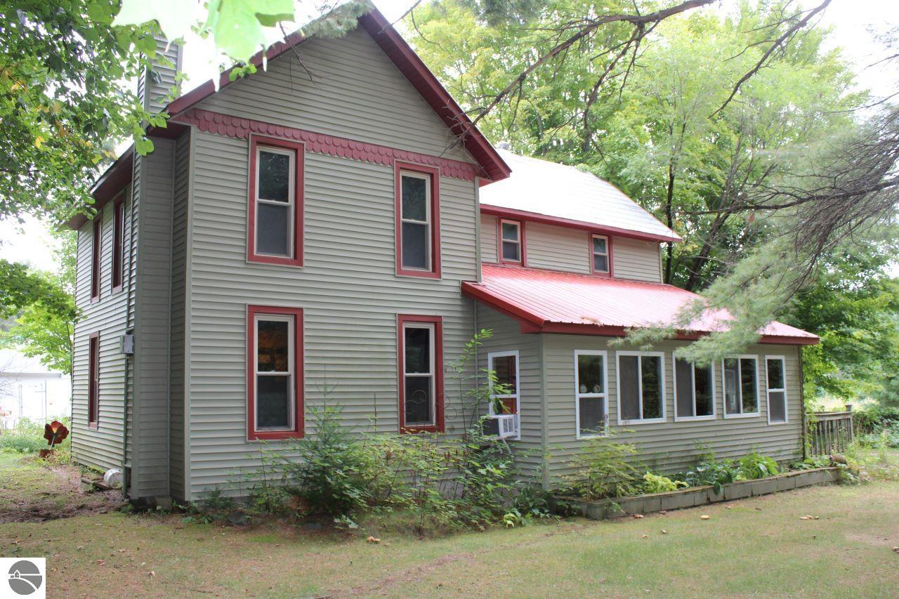 Two-story gray house with red trim and a long enclosed porch beneath leafy trees.
