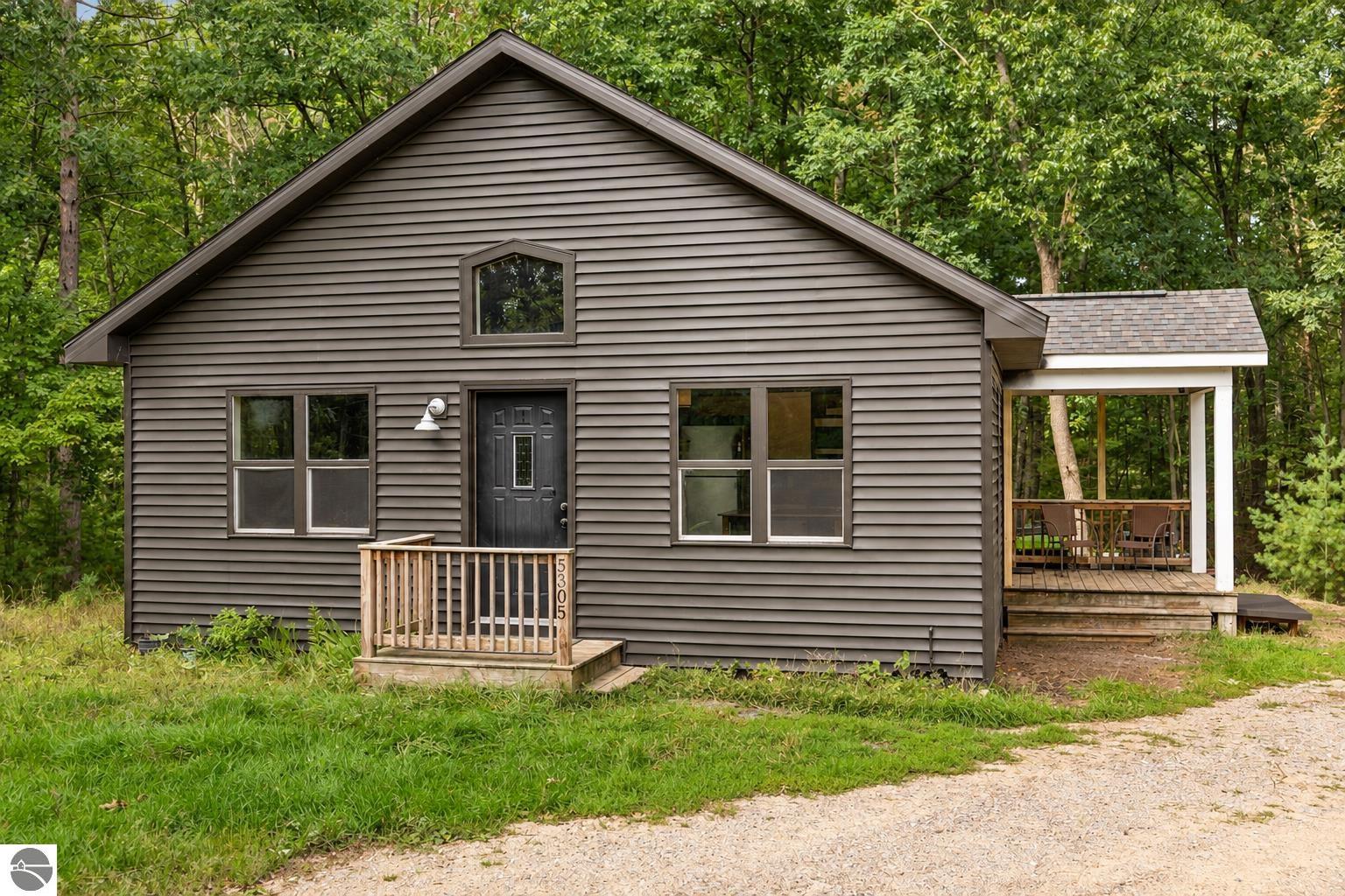 Gray gabled home with a small front porch and covered deck surrounded by trees.