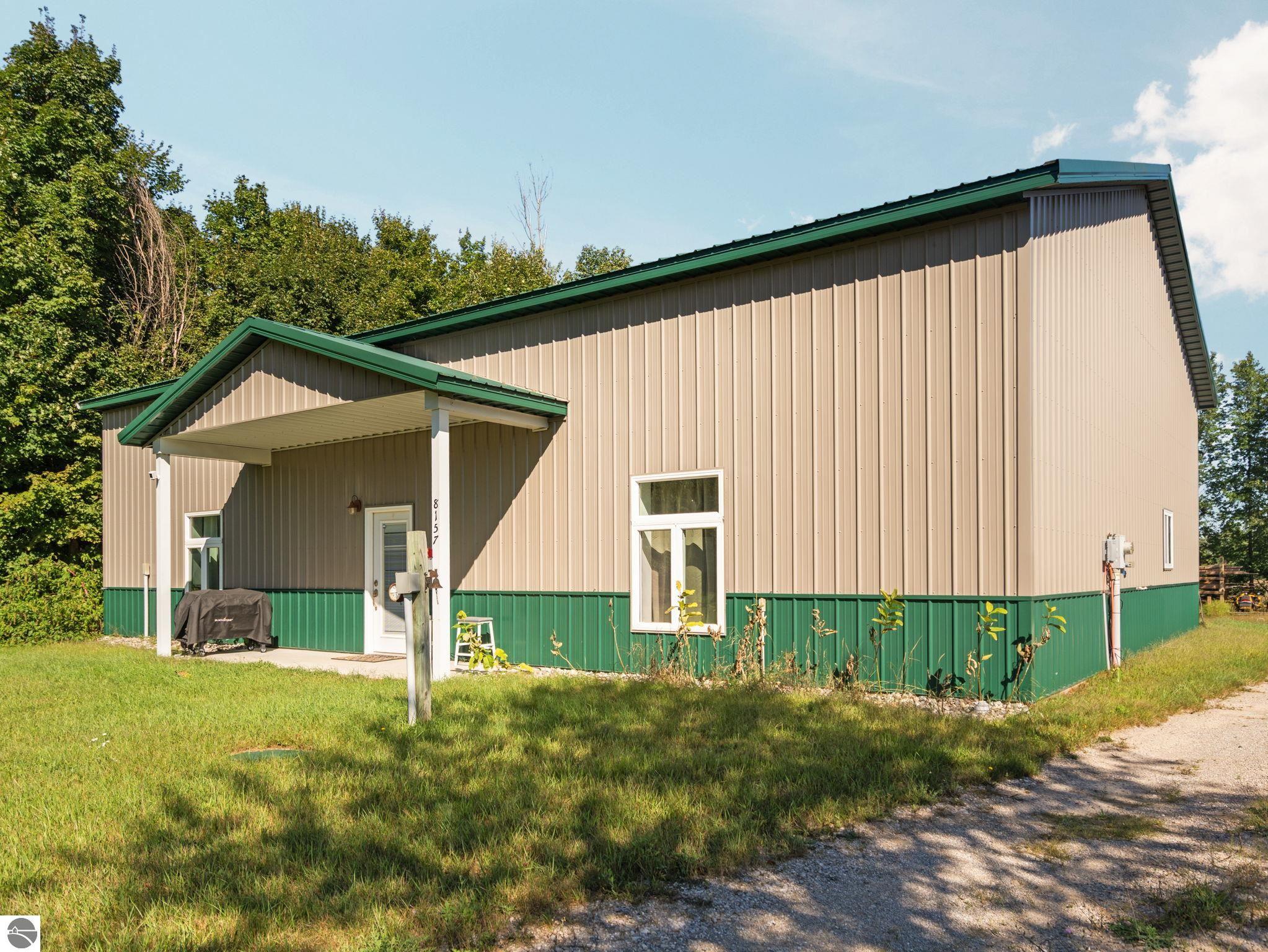 Beige metal-sided building with green trim, covered entrance, and gravel drive.