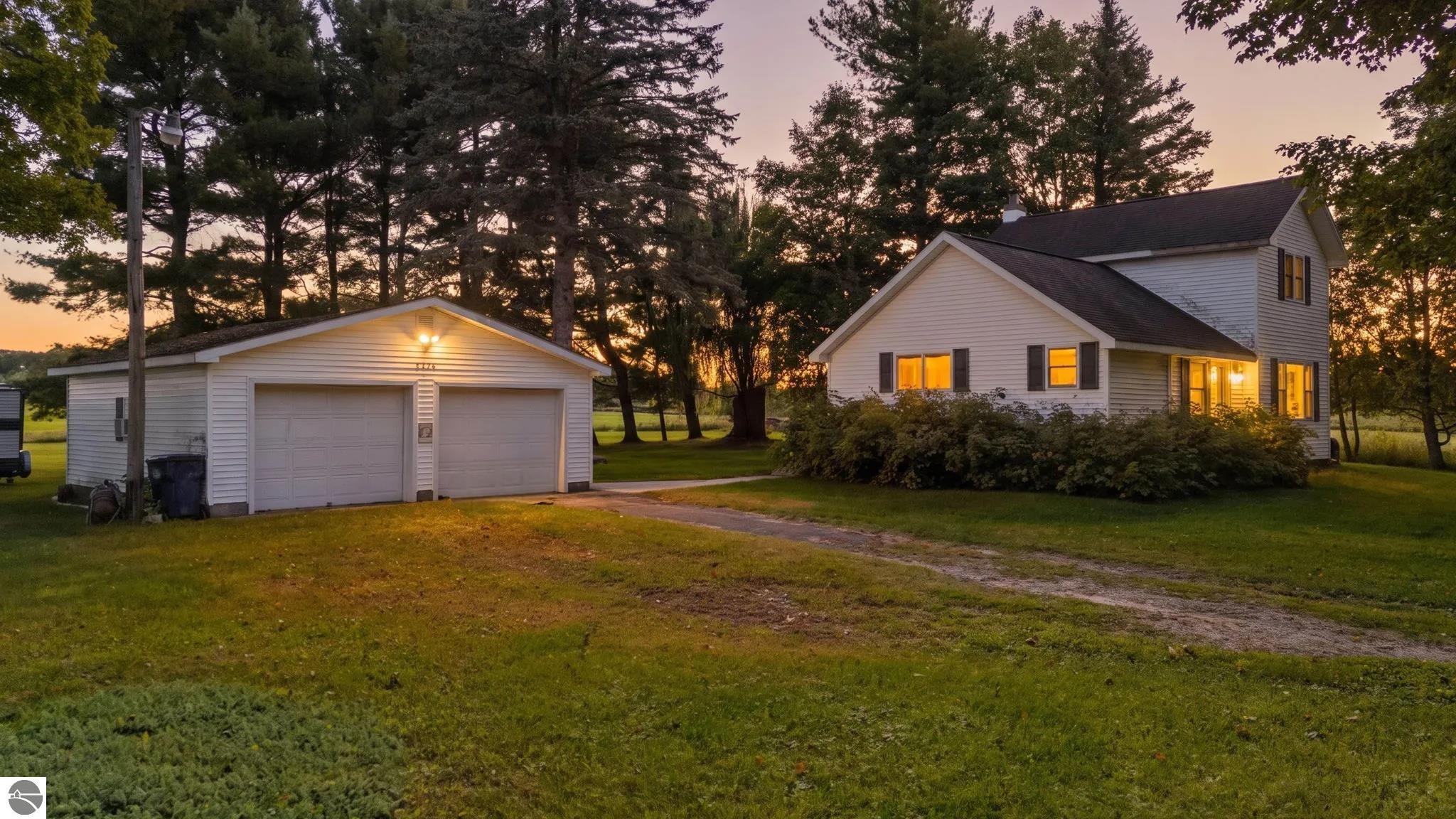 White two-story house with a detached double garage glowing warmly at dusk.