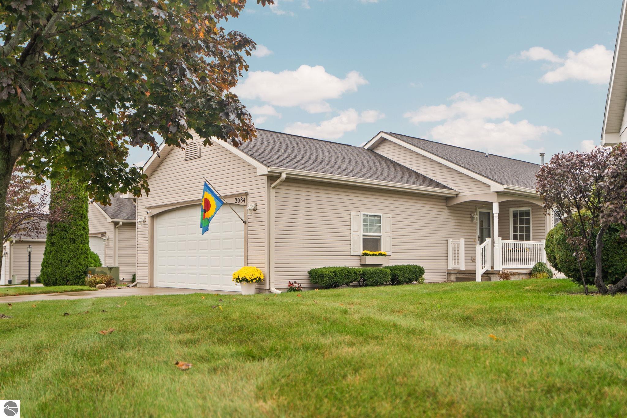 Beige single-story home with an attached garage, covered porch, and colorful flag by the garage.