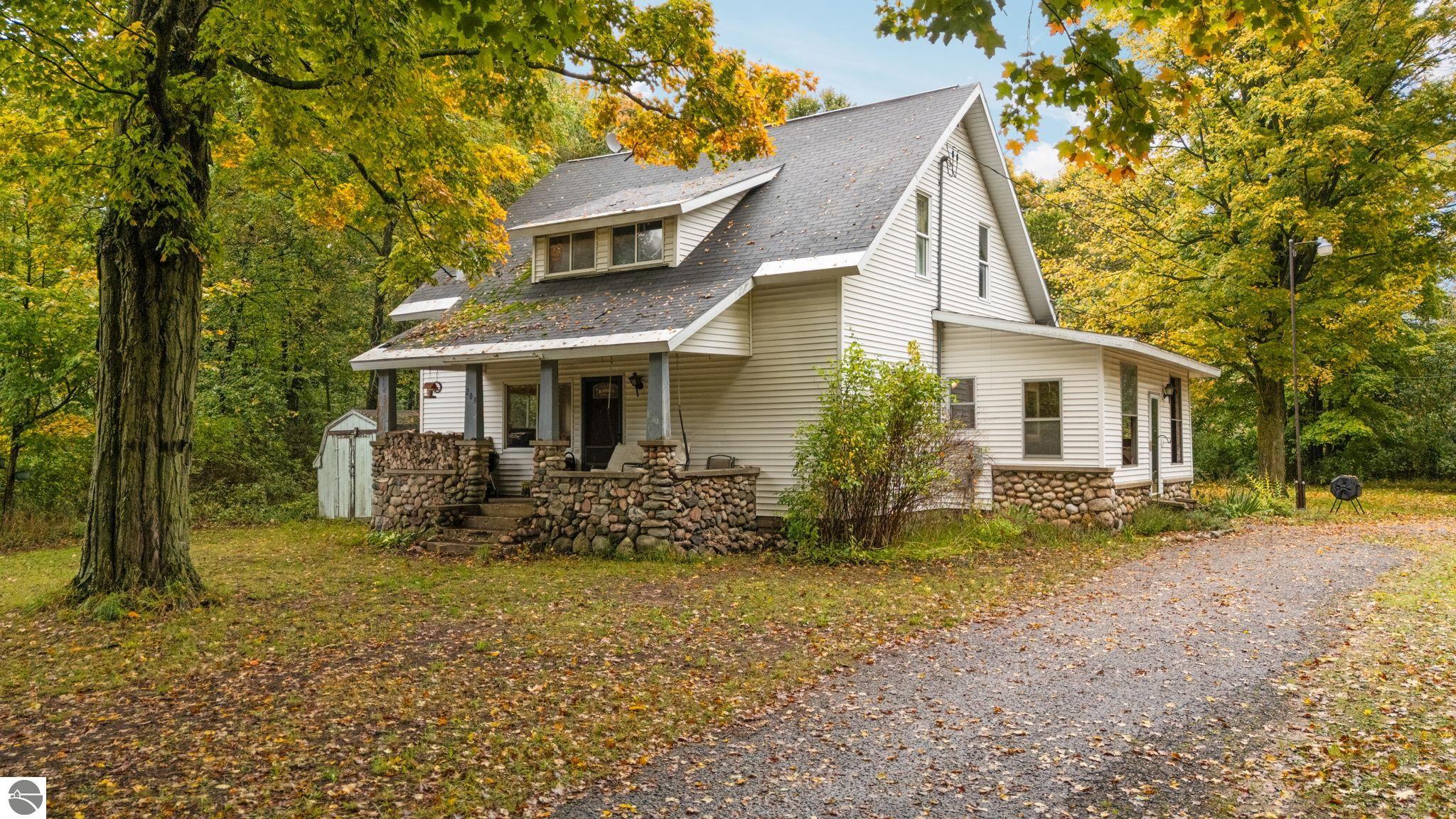 White two-story house with a stone porch, surrounded by yellow autumn trees.