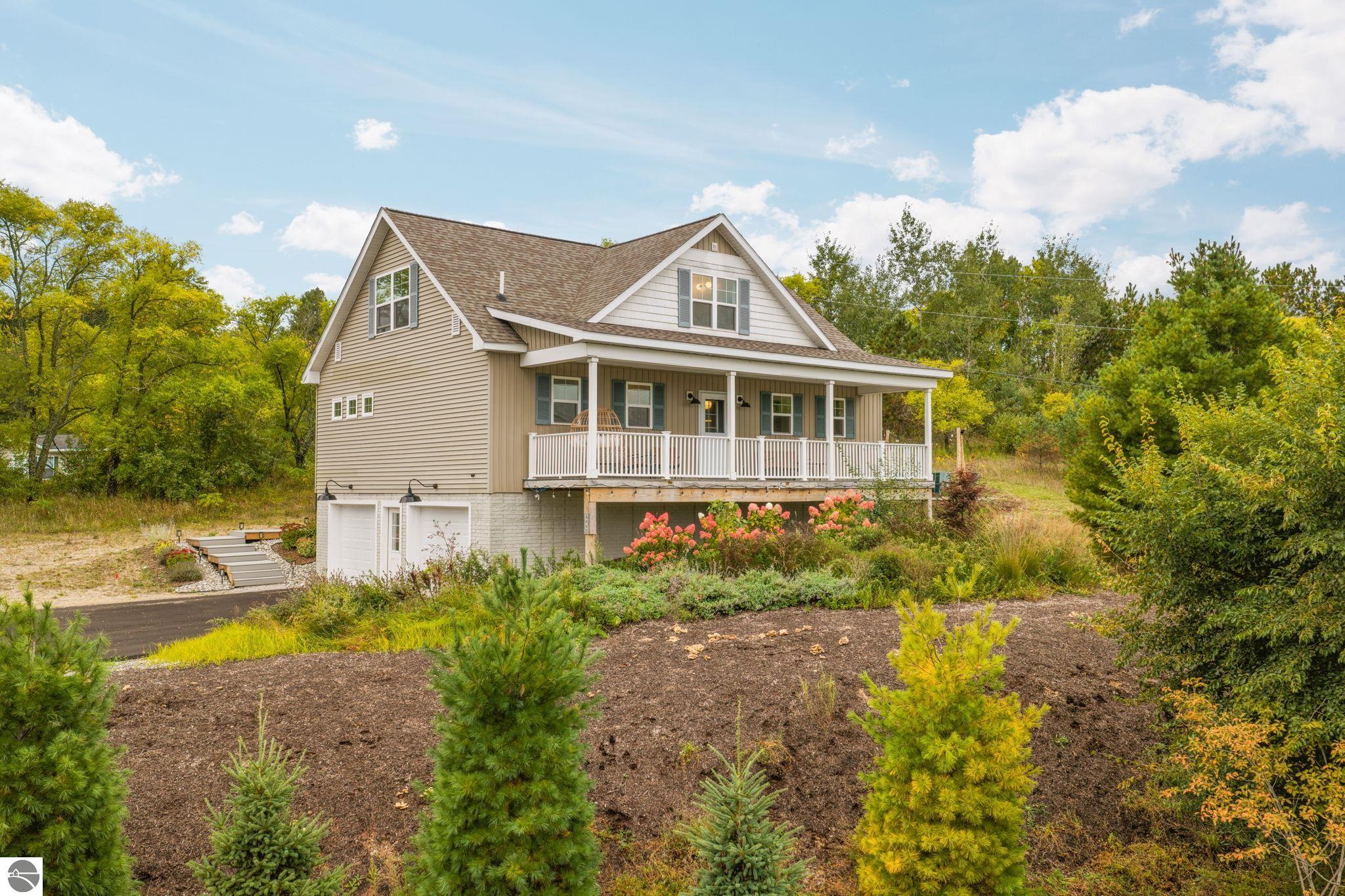 Beige two-story home with a covered porch, attached garage, and landscaped yard.