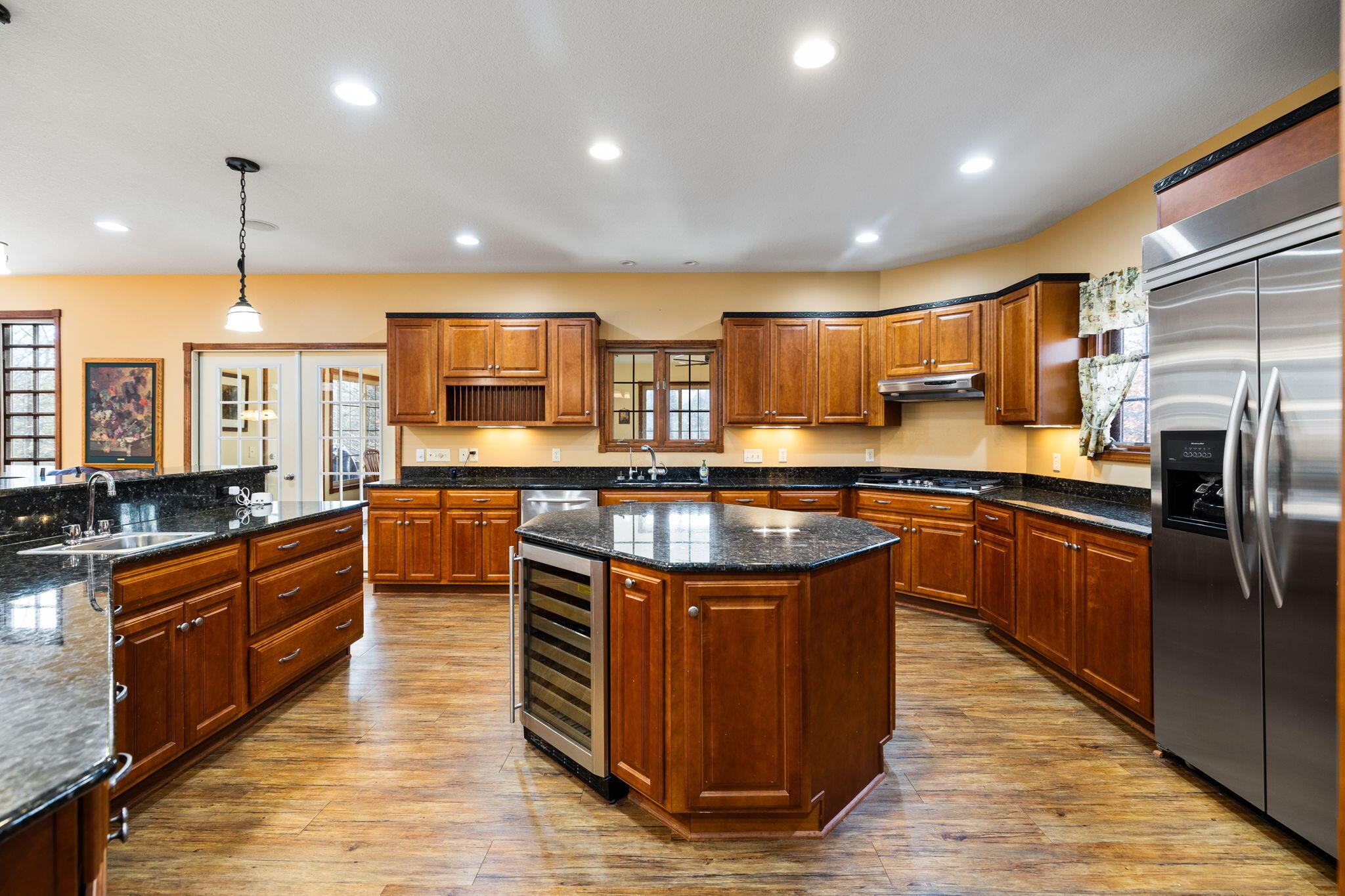 Kitchen with a large granite island, rich wood cabinets, and stainless steel refrigerator.