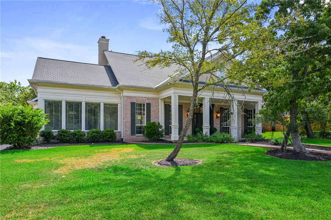 Brick-and-siding house with a covered porch, gray roof, and mature trees across the lawn.