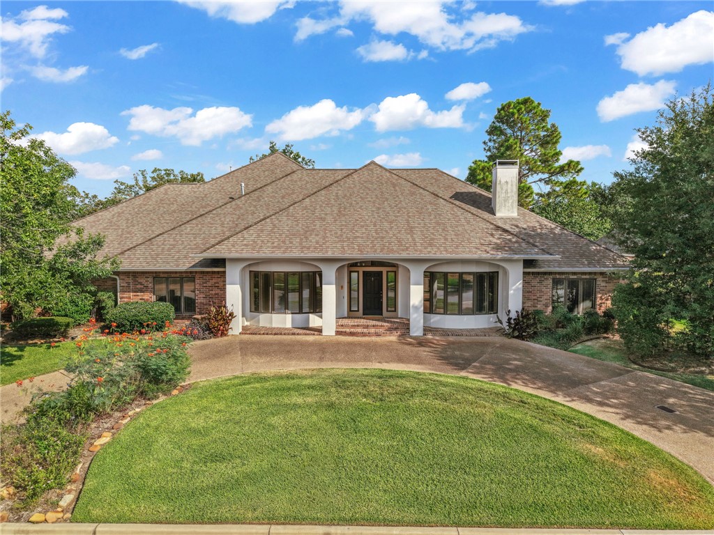 Single-story brick home with an arched entry, curved driveway, and landscaped lawn.