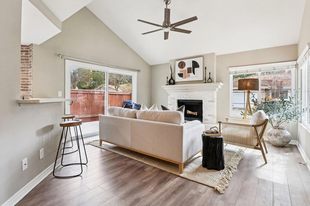 Staged living room with vaulted ceiling, white fireplace, and sliding doors to a fenced backyard.