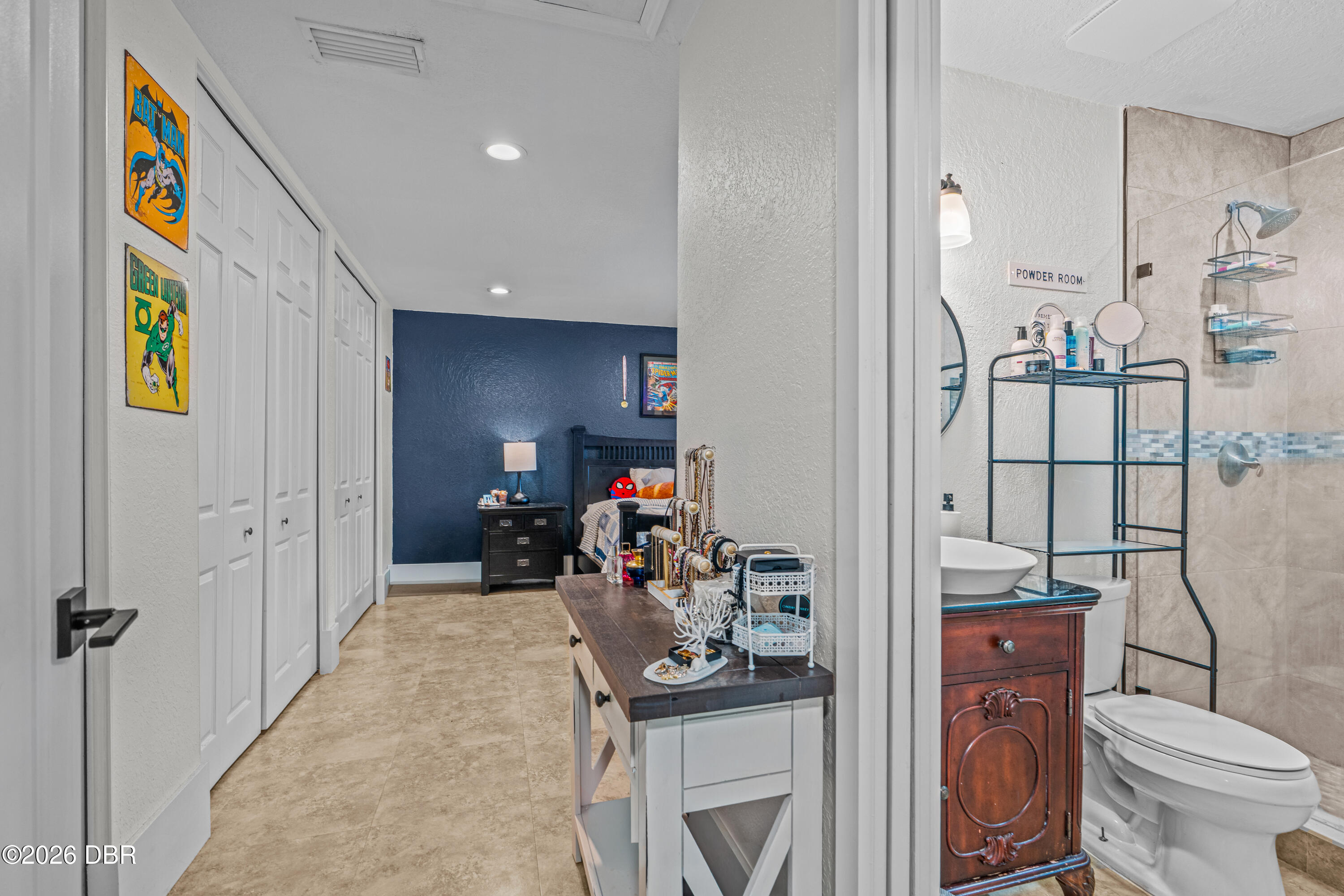Bedroom and adjoining bathroom with a navy accent wall, superhero posters, tiled shower, and ornate wood vanity.
