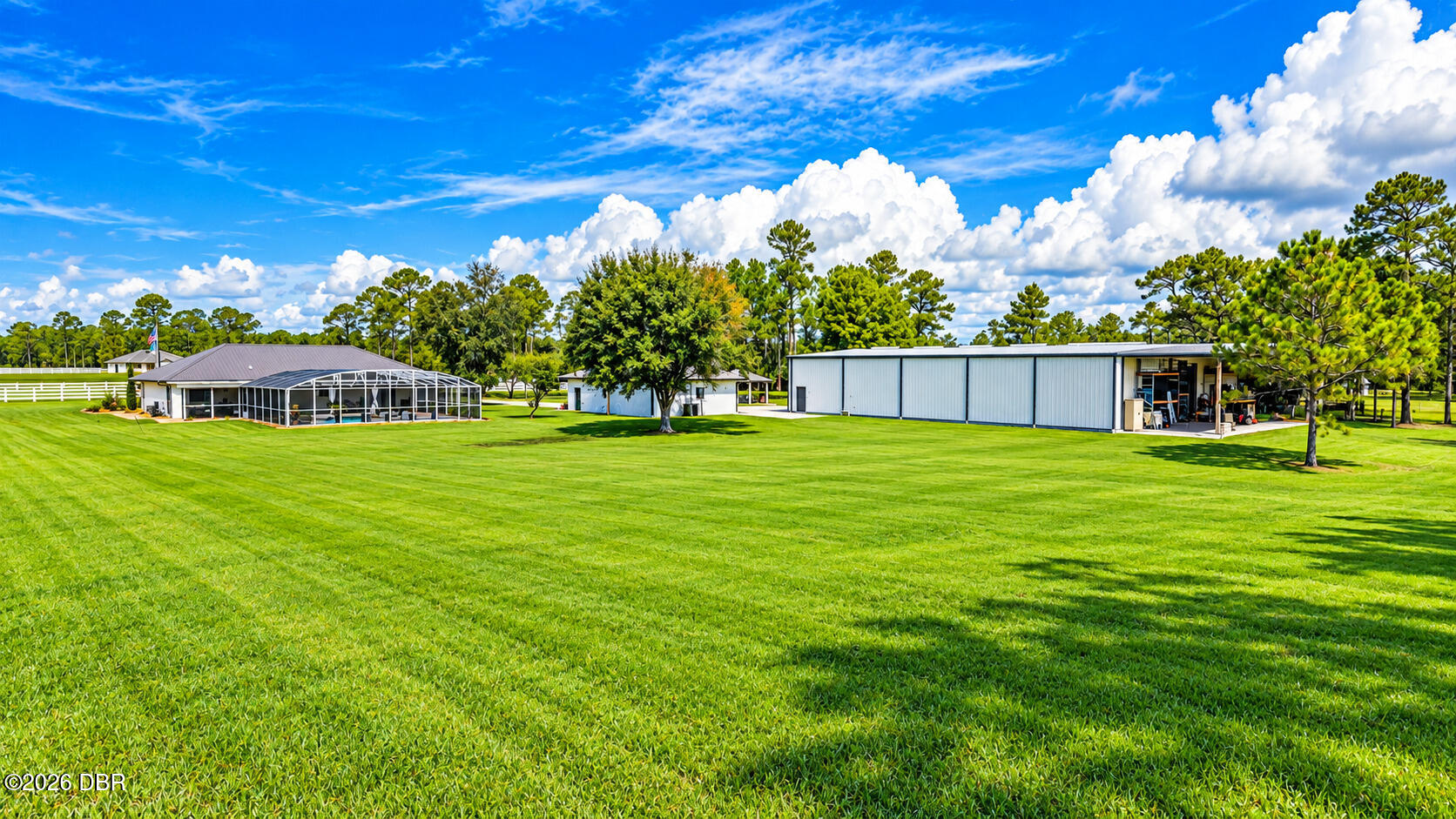 Panoramic property grounds with a screened pool enclosure, large metal outbuilding, and expansive lawn.