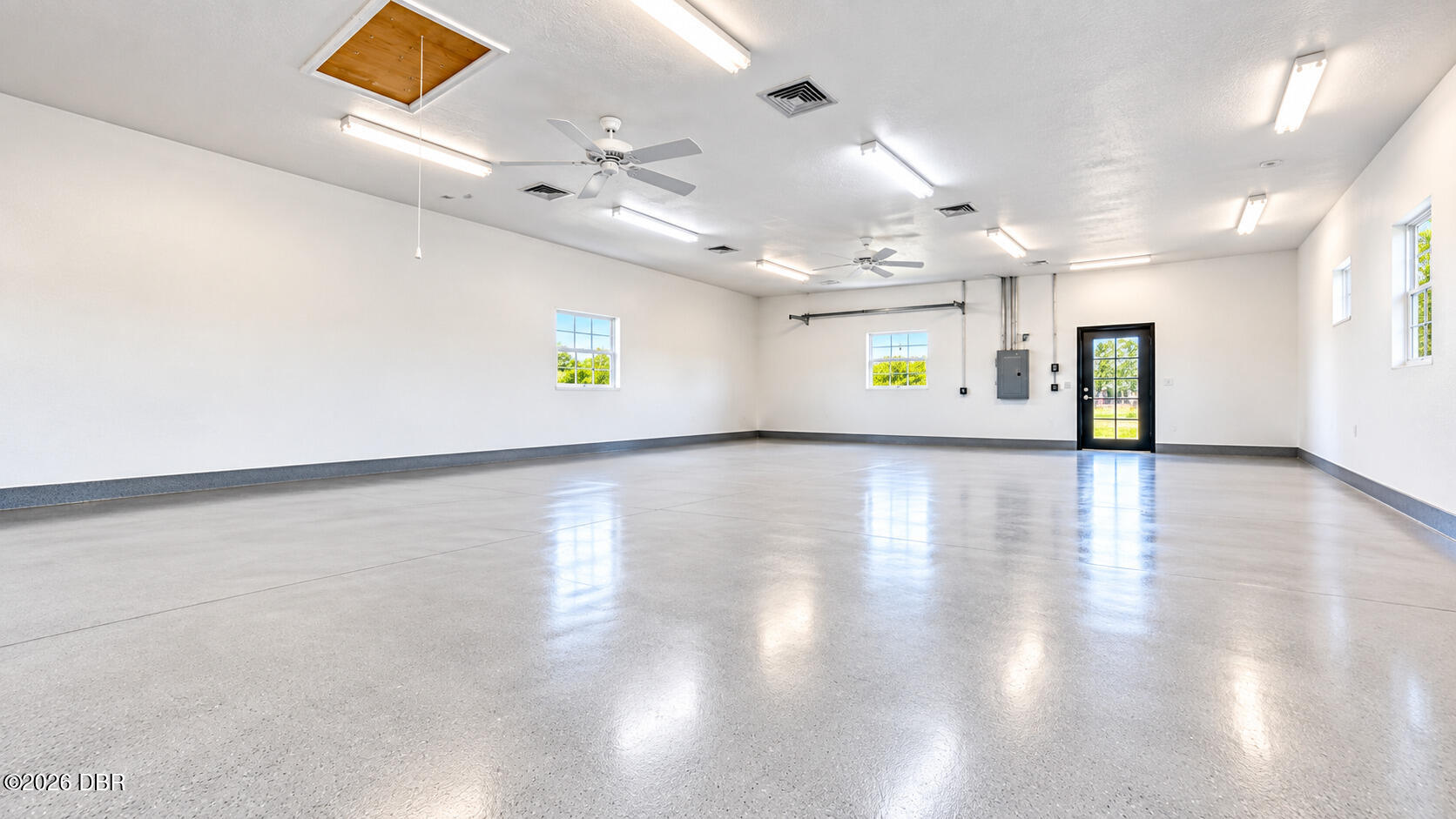 Spacious empty garage with a polished concrete floor, multiple windows, and ceiling fans.