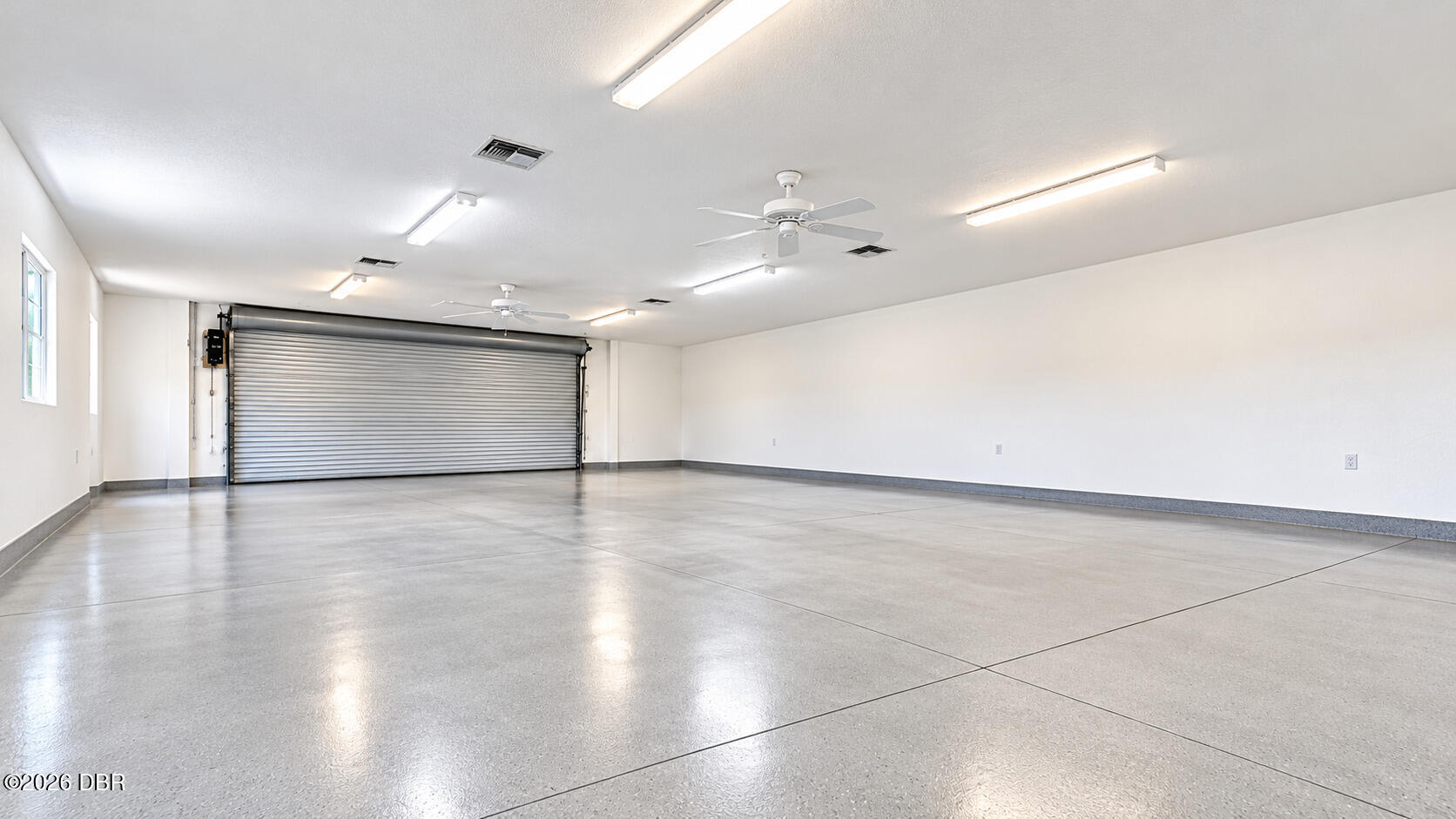 Empty garage with a polished concrete floor and wide metal roll-up door.