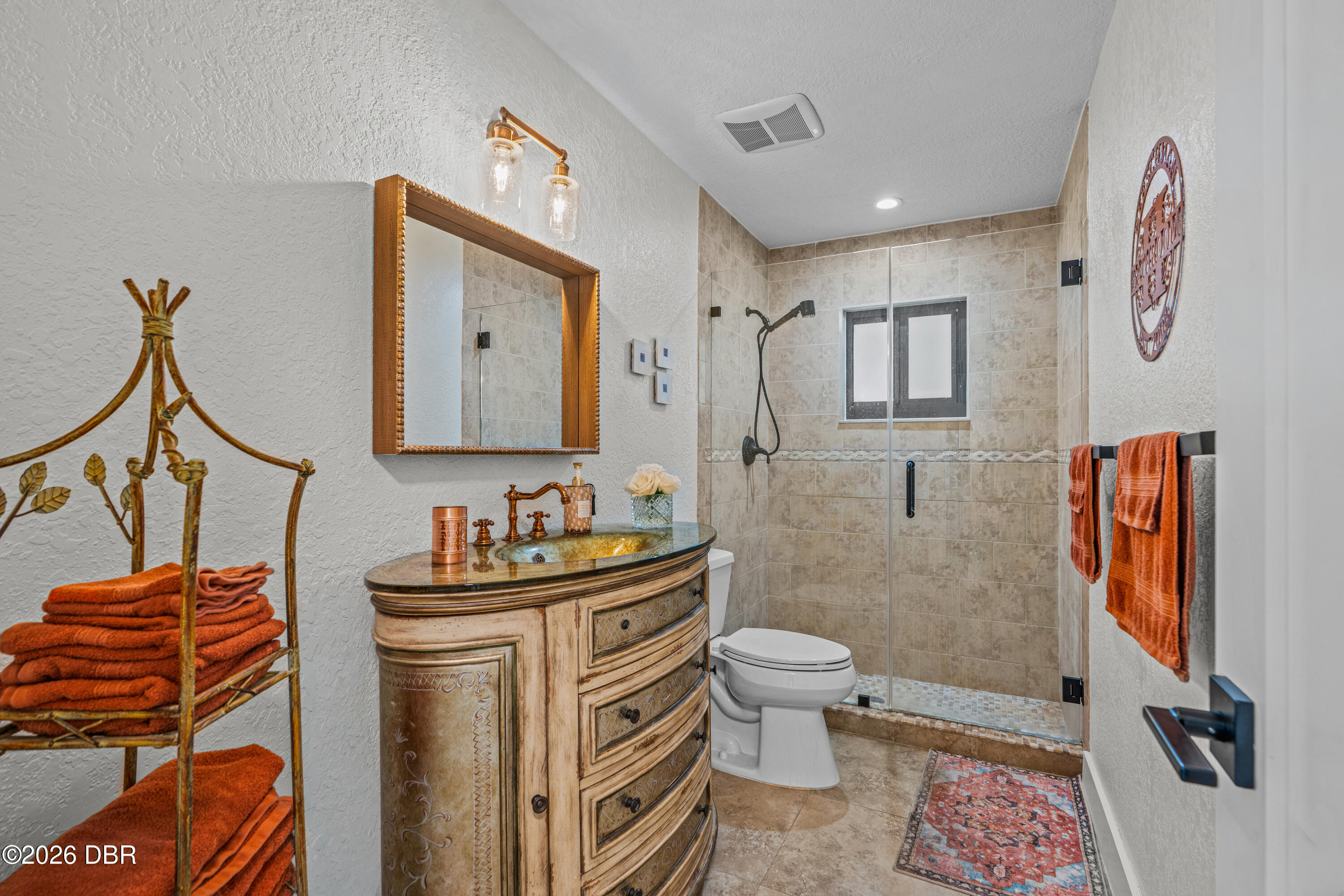 Bathroom with ornate wood vanity and vessel sink beside a tiled, glass-enclosed walk-in shower.