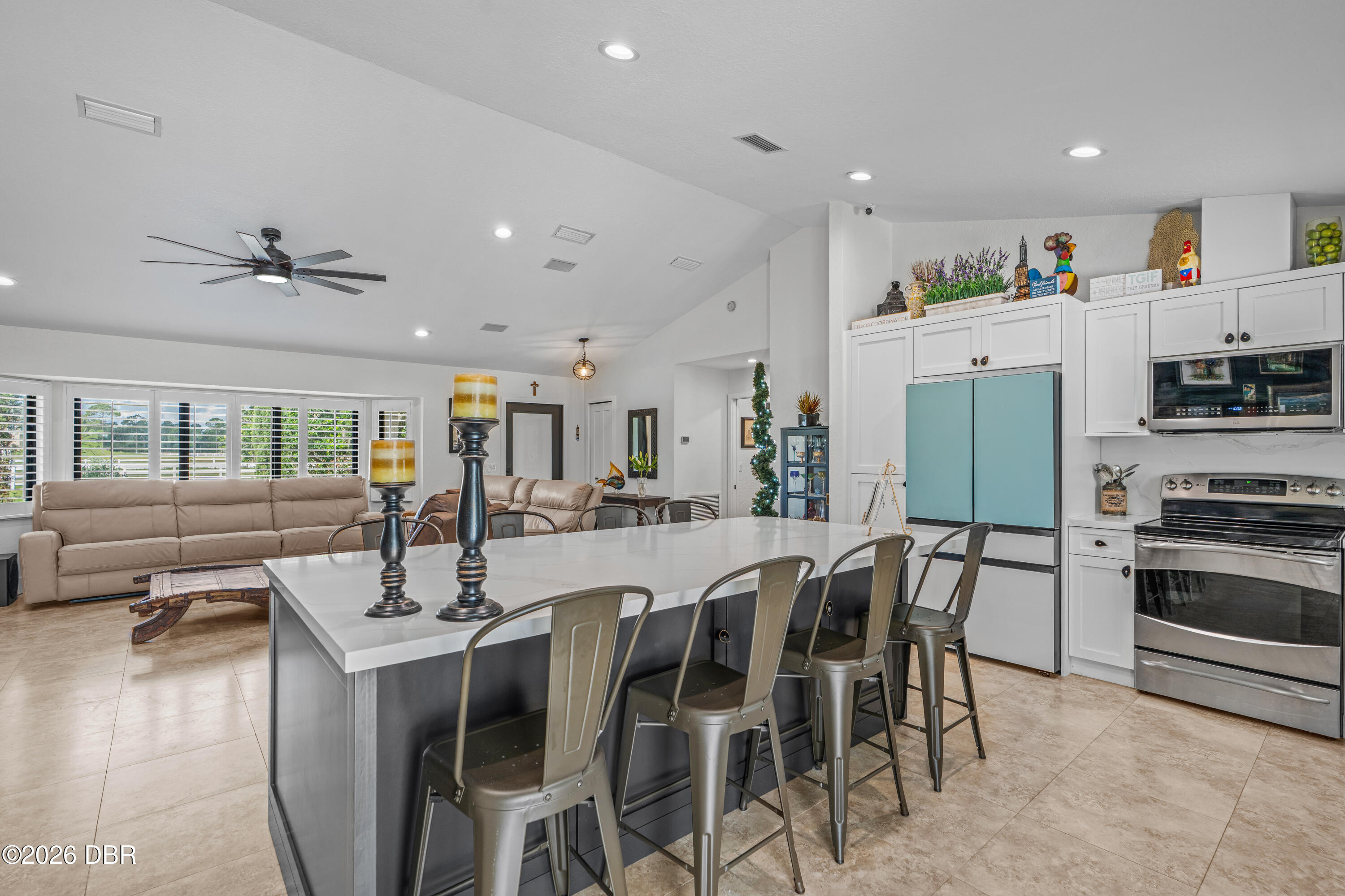 Open-plan kitchen with a large white island, turquoise refrigerator, and adjoining beige living-room sectional.