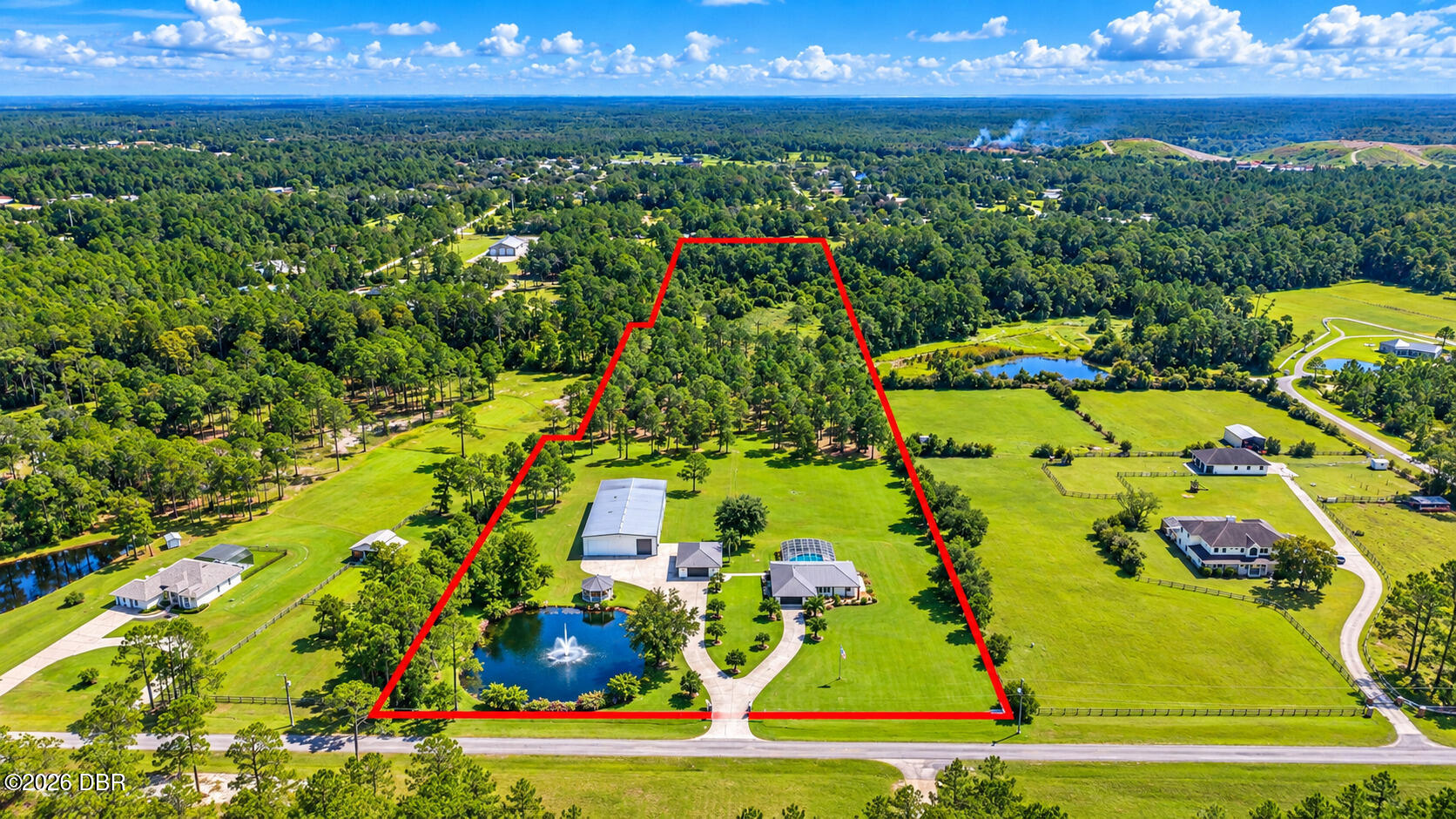 Aerial view of the red-outlined property, showing a home, outbuildings, pool, fountain pond, and wooded acreage.