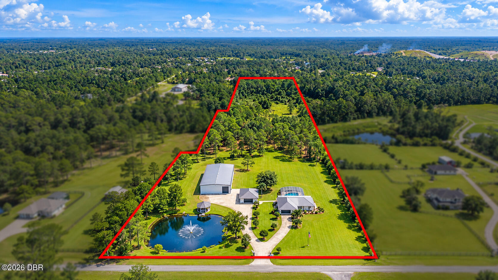 Aerial view of a wooded estate outlined in red, with several buildings, a pond, and a swimming pool.
