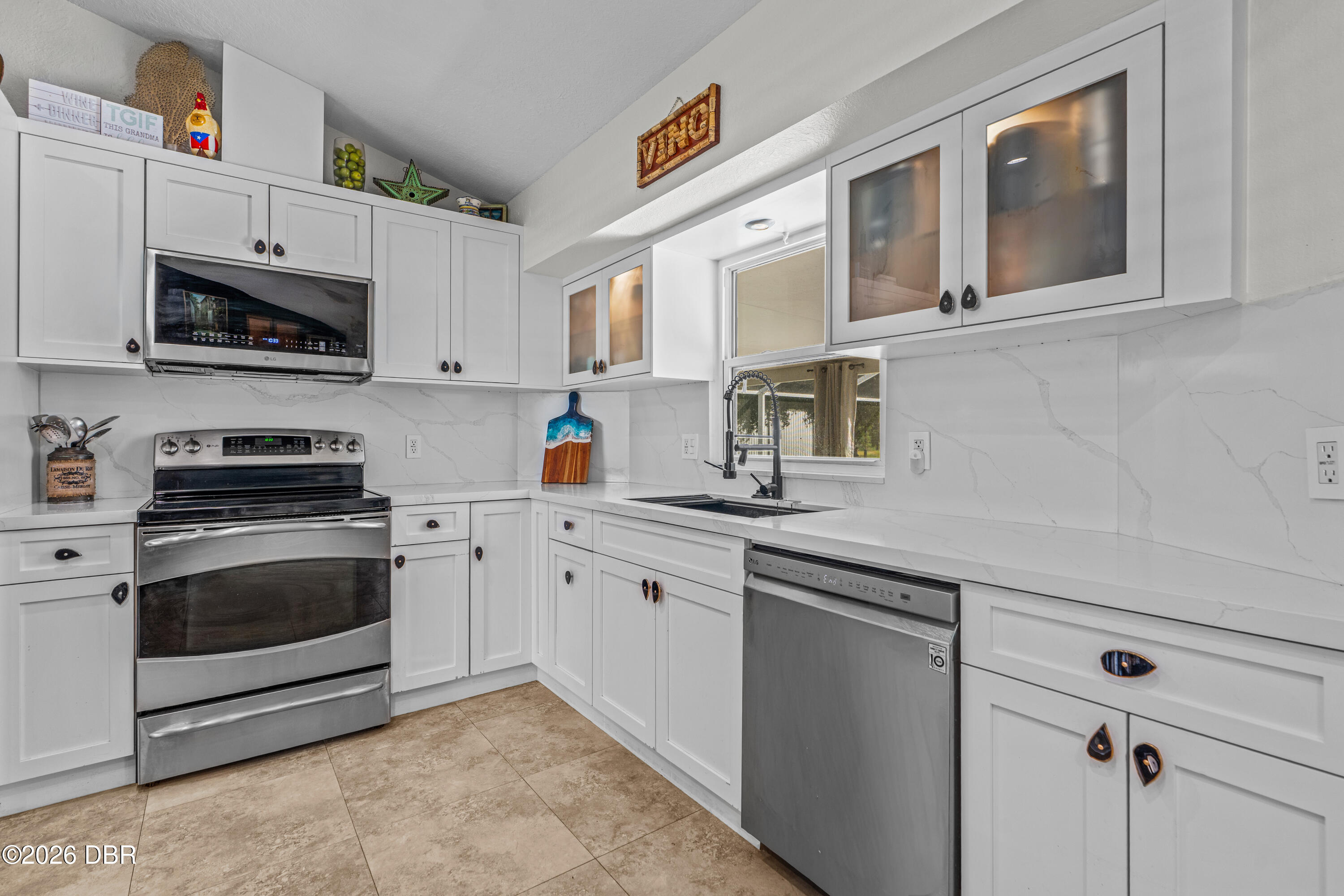 Kitchen with white shaker cabinets, veined counters, stainless steel appliances, and a window above the sink.
