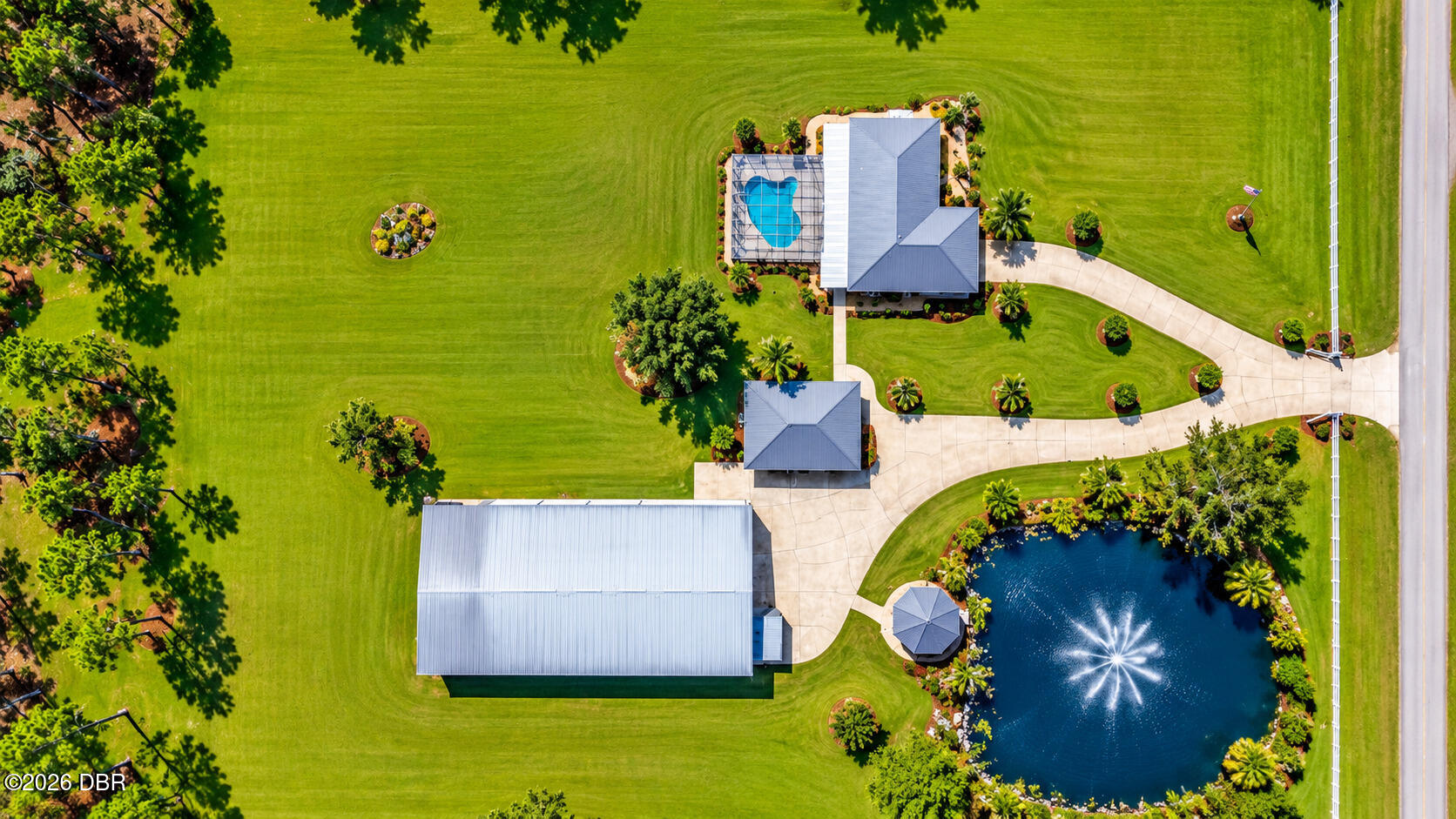 Aerial view of a landscaped property with a home, pool, large outbuilding, and fountain pond.