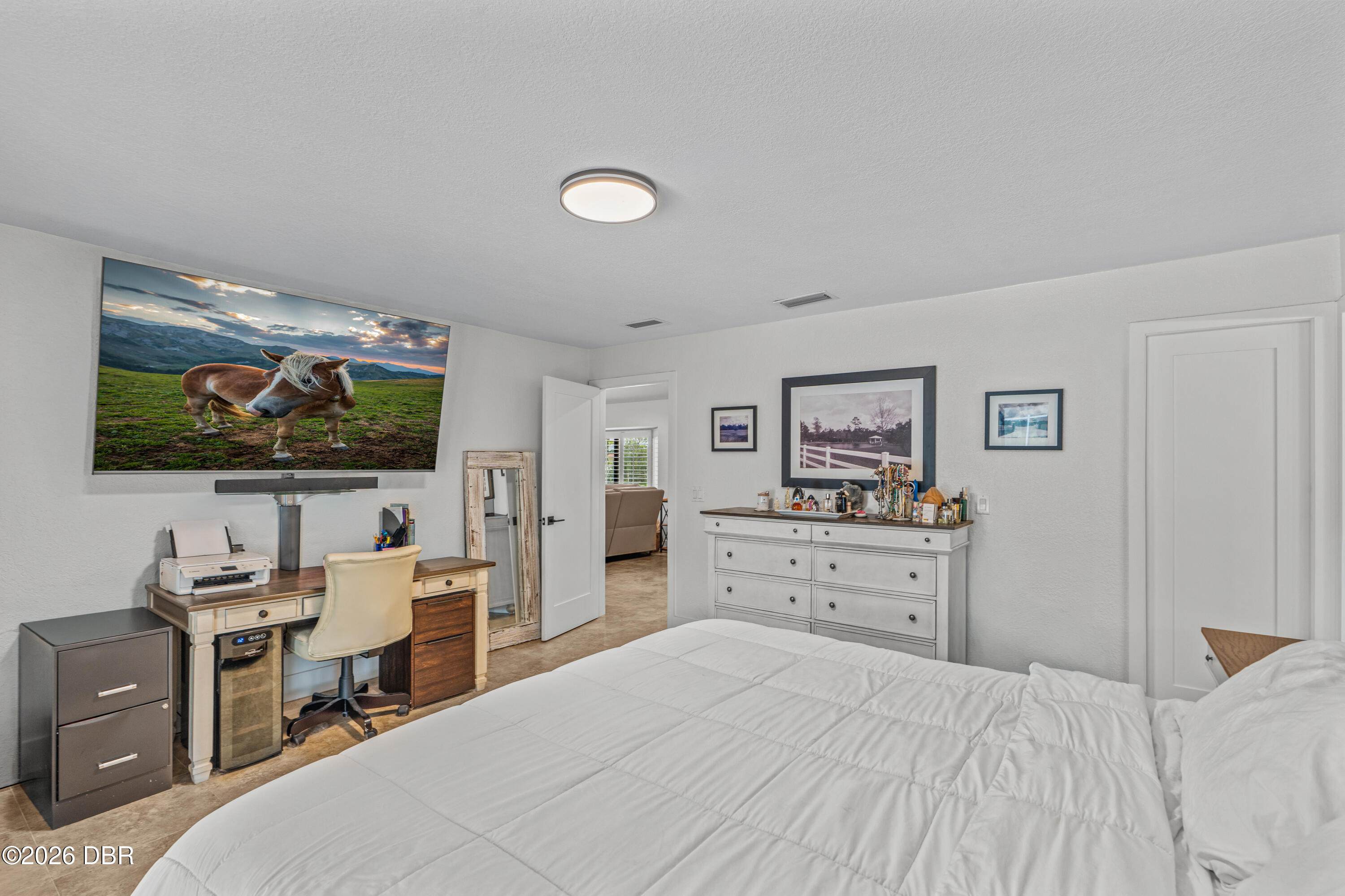Furnished bedroom with a white bed, desk beneath a horse-displaying television, and white dresser.