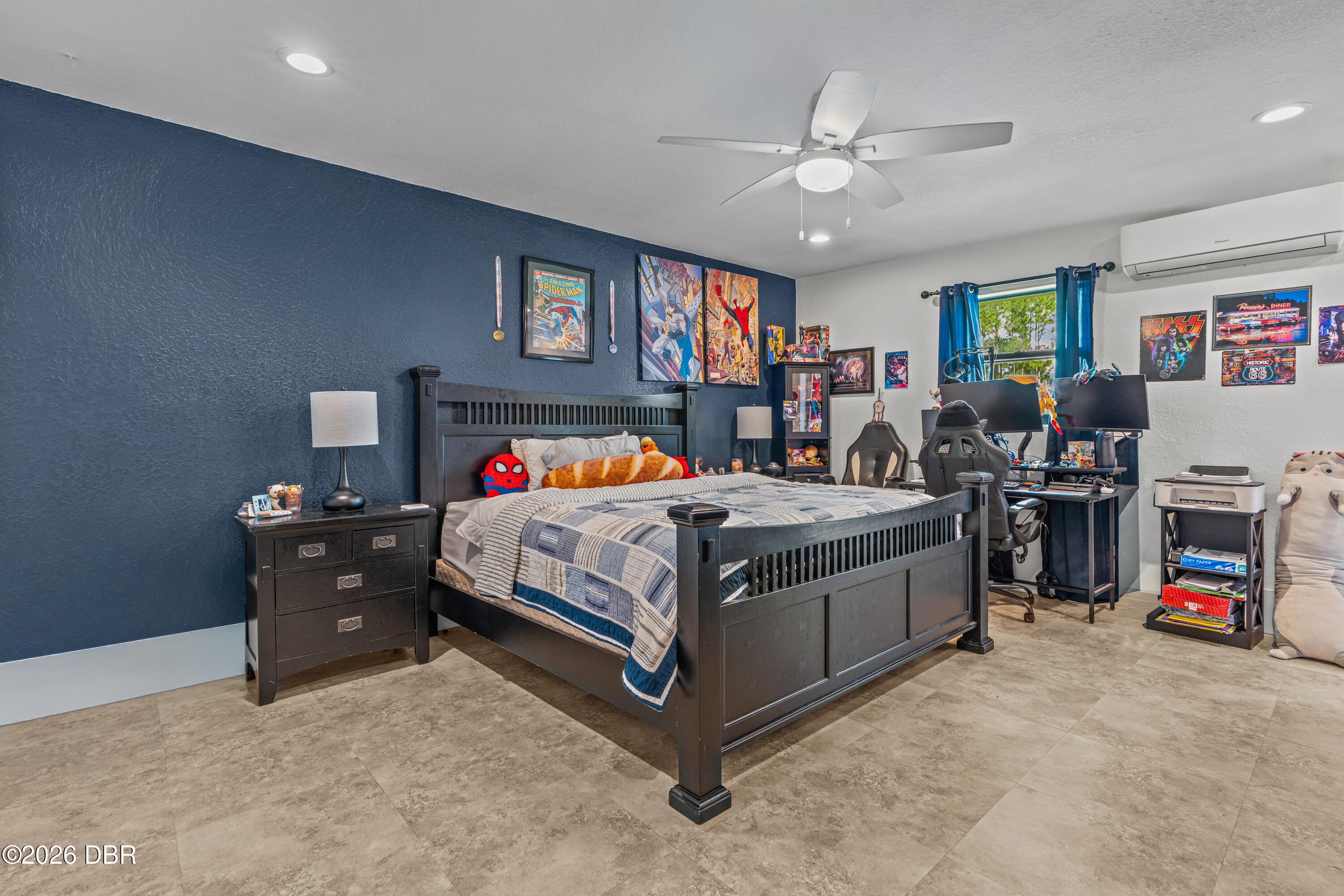 Bedroom with a dark wood bed, navy accent wall, comic posters, and a dual-monitor gaming desk.